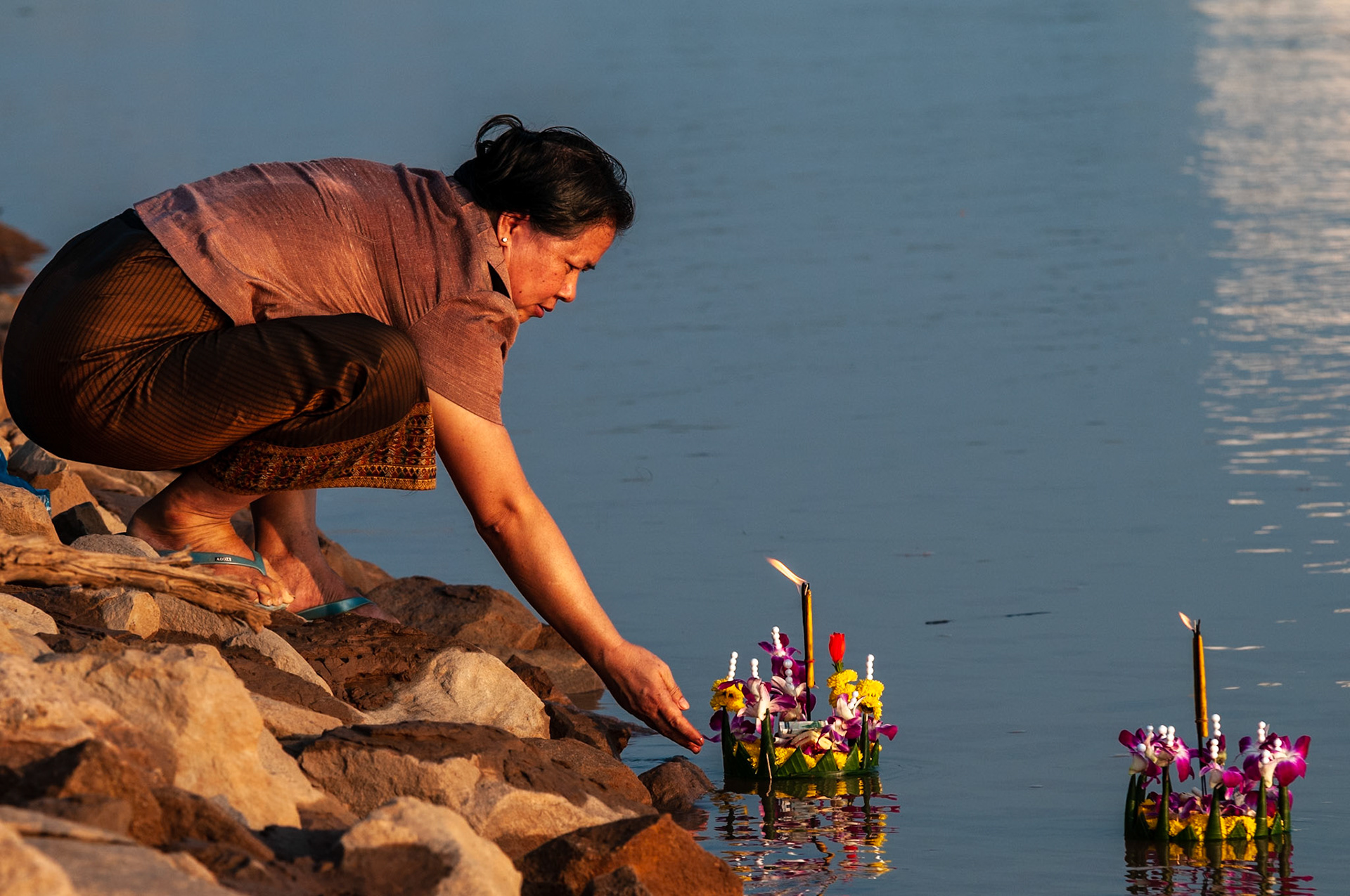 Celebrations take on a carnival feel as Boun Lai Heua Fai boats light up the Mekong River. Families bond over the tradition of floating small boats carrying offerings down the river. The boats are made from woven banana leaves and are decorated with candles and flowers. People pay respect to the Mekong, the Mother River, for providing water and strengthen their connection with her, asking for blessings and good luck.
