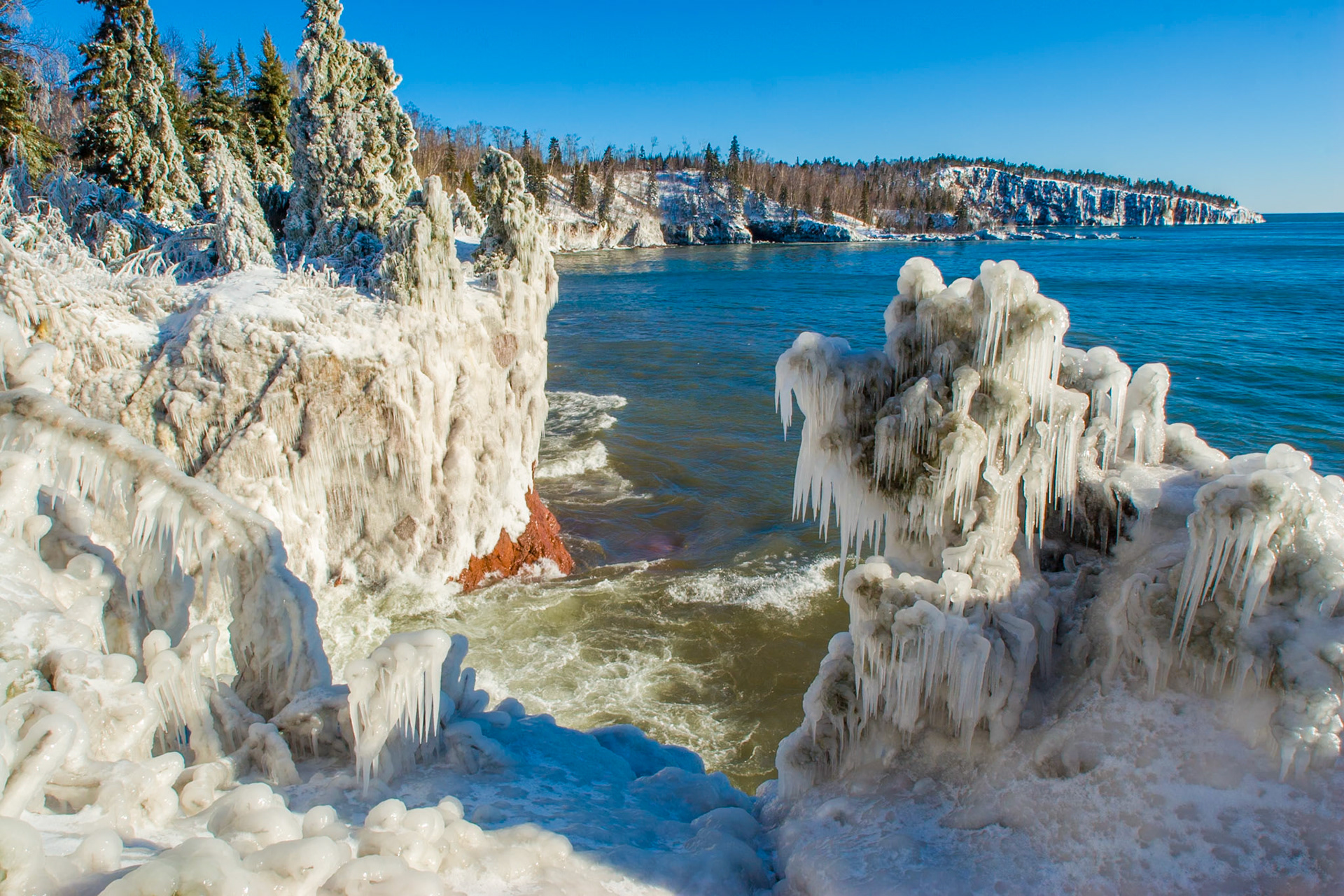 March 13 – Cliff IceMid-March is the battle of the seasons along Lake Superior.After the waves rage, the icy aftermath clings to trees and cliffs in spectacular beauty. There is no better place to witness this artistry than Tettegouche State Park.Cold fronts still pack a punch. Freezing mist from crashing waves coats the shoreline in God’s glorious design.The storms have had their way, but this ice will not last long in the powerful afternoon sun. Soon, the icicles will melt back into the waters—ready for the next storm.“From whose womb comes the ice?Who gives birth to the frost from the heavenswhen the waters become hard as stone,when the surface of the deep is frozen?”— Job 38:29–30It is often after the roughest storms that the starkest beauty appears.Like these trees bowing under the weight of ice, bow before the Lord—and in time, you will feel the warmth of the Son of God.