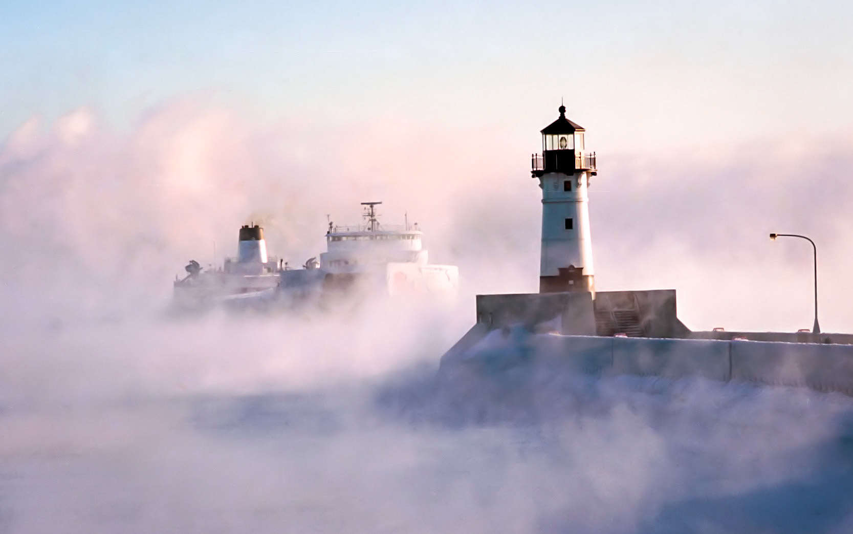 January 12 - Ghost ShipLake Superior lets off steam as an ice-covered Laker enters the Duluth Shipping Canal on a freezing January morning. Fingers freeze, and camera batteries die quickly in this weather, so quick snapshots are the rule of the day. There are a few days of Duluth's year when conditions are right for thick sea smoke, but those challenging days make for some beautiful images.All three forms of water are visible here: steam, liquid, and ice.The swirling fog, icy-cold steel, and soft light combine to chill you to the bone while warming the spirit. Winter is the master season for photography in the Northland.By the breath of God ice is given, and the broad waters are frozen fast. Job 37:10Winter strips the world to its essentials—cold, light, and breath. In that simplicity, the presence of God becomes easier to see.