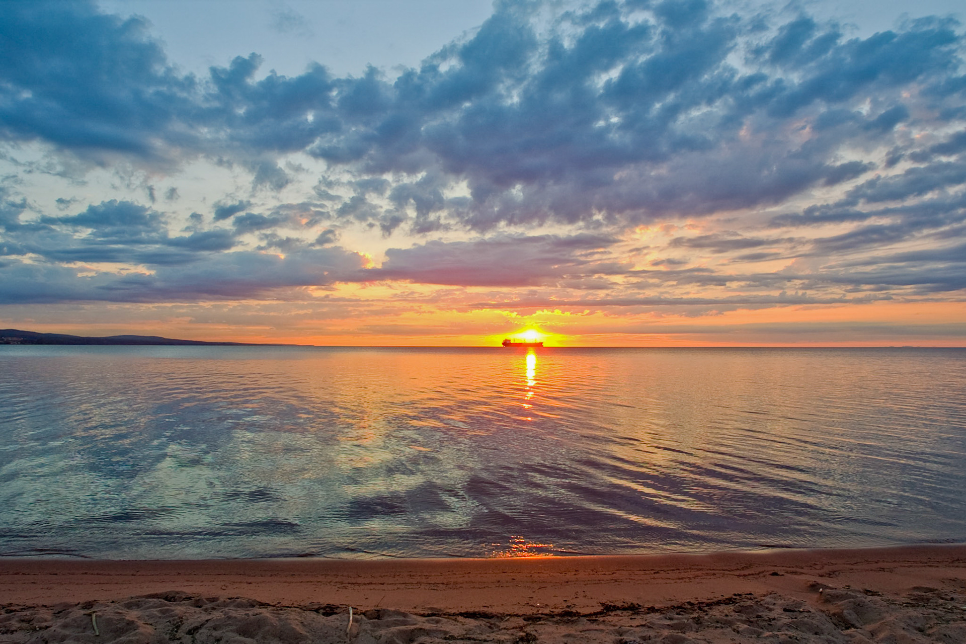 August 3 - Freighter in the Sunrise - A quiet early morning stroll along Park Point Beach often develops into a photo opportunity.Here, a ship waits at anchor for its turn to load grain.During the first weeks of August, Lake Superior is the quietest time of year on the shores of the big lake and an excellent time for a long walk.Better is a handful of quietness than two hands full of toil and a striving after wind. Ecclesiastes 4:6