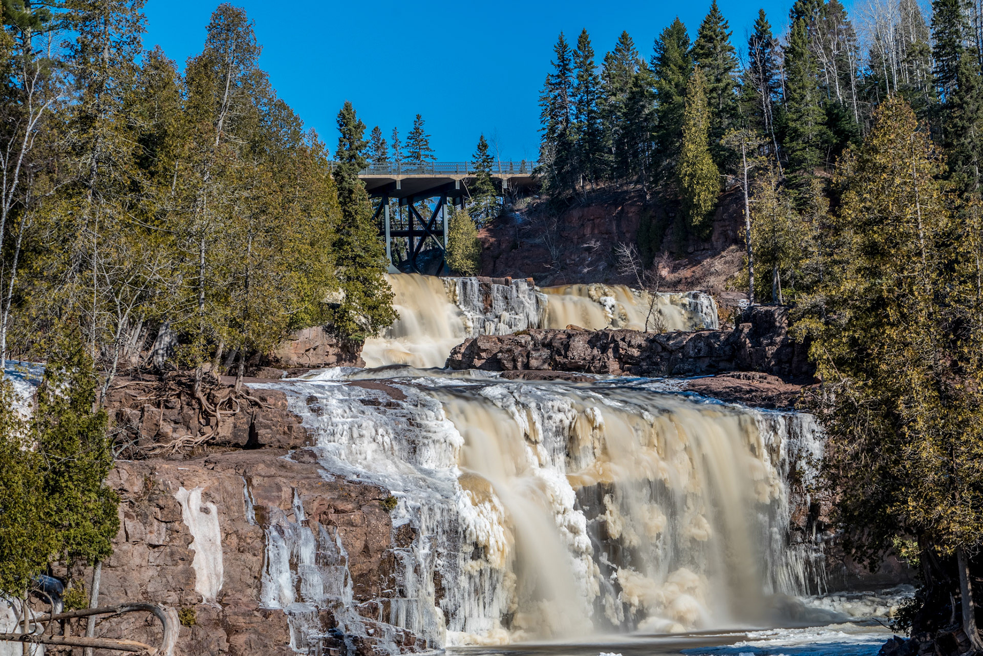 April 8 - Frigid Gooseberry FallsGooseberry Falls, still showing remnants of winter, is being charged up with the beginning of spring runoff. Over the next few weeks, meltwater will gorge the river valley with tremendous amounts of water from melting snow in the inland swamps and spring rains. The freshwater brushing past dissolves the remnant of underlying ice left over from winter.The water finishes its trip into Lake Superior and replenishes the big lake for another summer."Deep calls to deep in the roar of your waterfalls; all your waves and breakers have swept over me." - Psalm 42:7Springtime is a time for hope and planning. All of summer lies ahead.