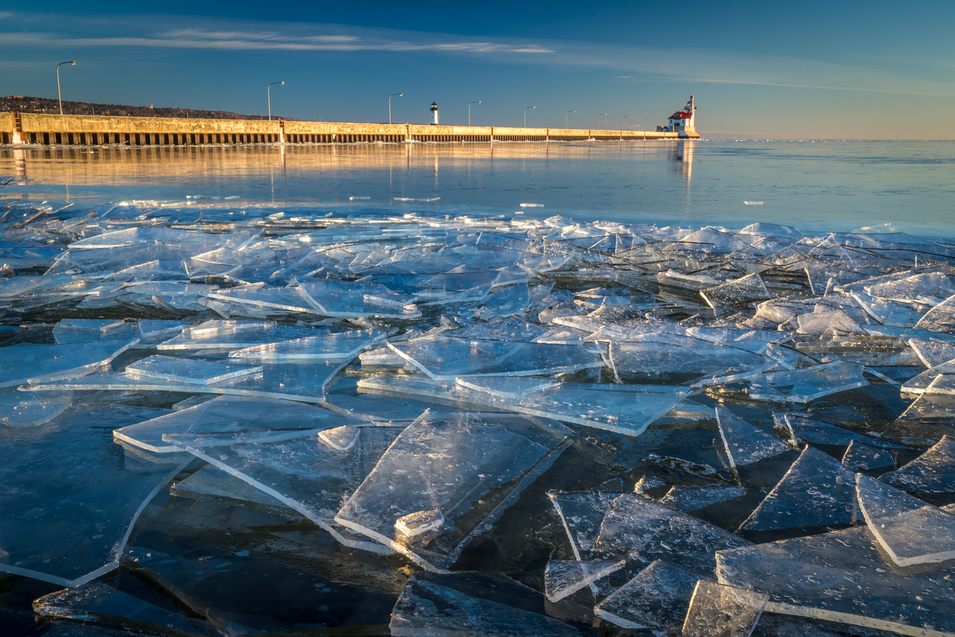 January 10 - Ice ShardsLayers of sheet ice piled up on the Park Point shoreline. The early morning light and clear blue sky set the scene for another perfect morning along the shore.Sheets of ice are broken up and stacked into piles by wind and currents along Lake Superior's shore. As I lay down in the snow to take this photo, I watched and listened as the shards moved and bumped against each other, sounding like a crystal chandelier.The scene was like a thousand others taking place on this day along Lake Superior. I felt blessed to have enjoyed midwinter in the cool Northland.By the breath of God, ice is given, and the broad waters are frozen fast. Job 37:10Sometimes you happen upon beauty; sometimes you have to search for it; and sometimes both happenstance and looking come together in the same place.