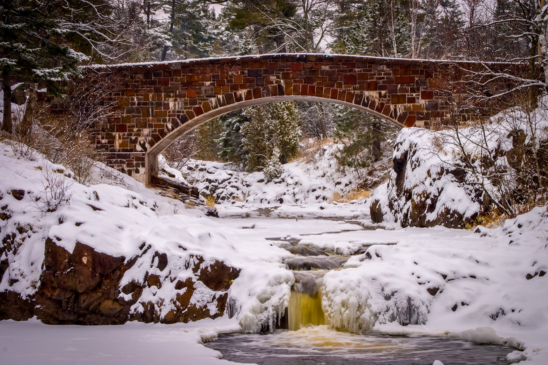 November 23 - Winter RiverLester River Stone Bridge. With winter right around the corner, local rivers, lakes, and streams begin to freeze and settle in for several months' rest under the ice.As winter takes hold, the landscape transforms into a winter wonderland. The peaceful stillness that accompanies the snowfall is only interrupted by the sound of the occasional bird chirping. It's a serene environment that makes you appreciate the beauty of nature in all its forms.From its chamber comes the whirlwind and cold from the scattering winds. By the breath of God, ice is given, and the broad waters are frozen fast. Job 37:9-10