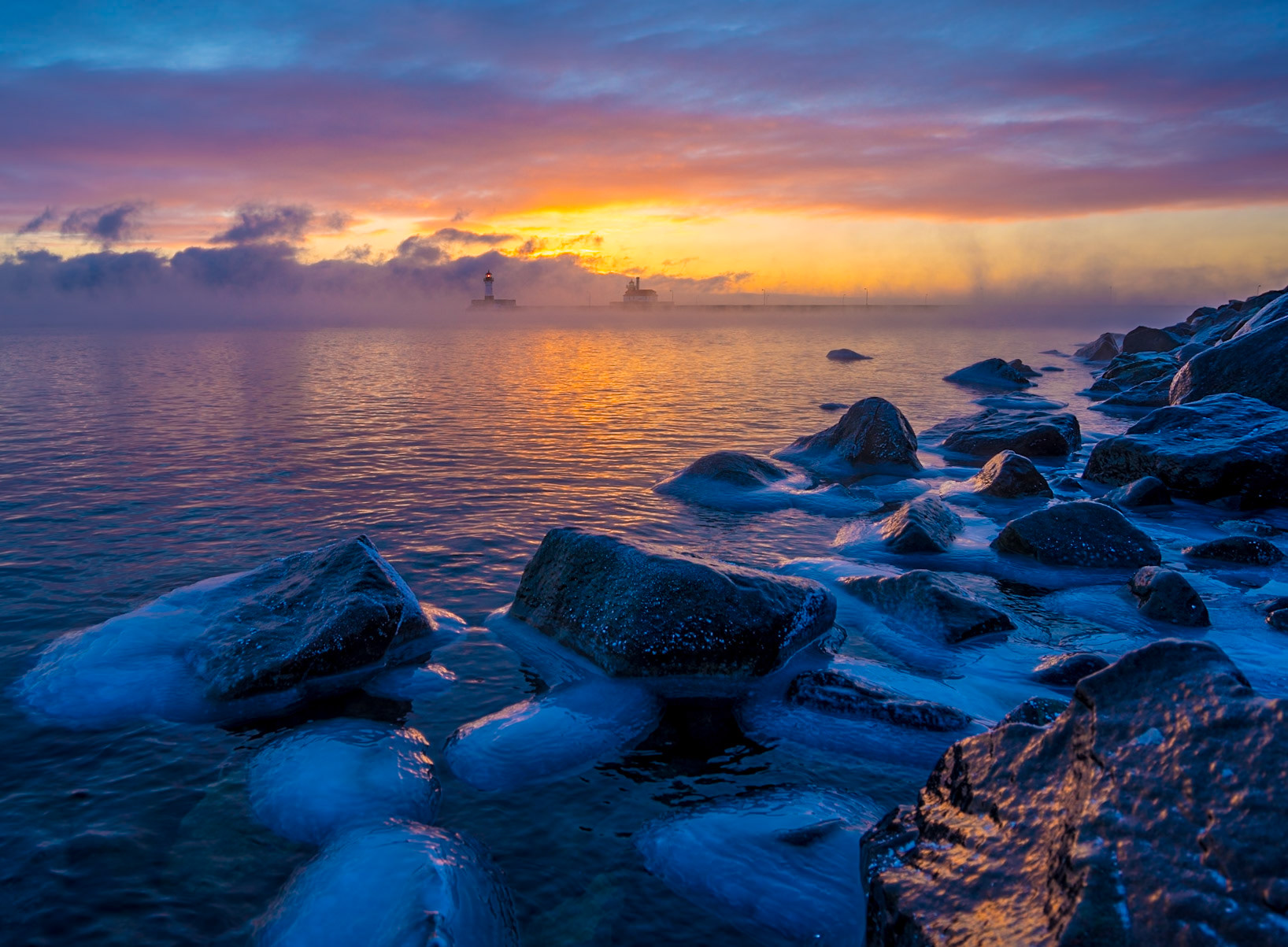 January 25 - Fire and IceWarm sunlight and ice-covered rocks blend, repeating a January scene across the Lake Superior shore. With the Duluth Lighthouse in the background, the sea smoke rising, and the colorful sunrise, it makes it worth a little sting of frostbite on the fingers.In deep winter, water appears in three states at once—ice along the shore, liquid lake water, and vapor rising as steam fog. As sunlight moves through this cold, moisture-filled air, it scatters and softens, blending ice, water, and light into a brief and beautiful winter display.January bursts with spectacular scenes that few people ever witness. Each day, God crafts these breathtaking moments for His pleasure, and occasionally, we get to enjoy them too. So teach us to number our days so that we may present a heart of wisdom to You. Psalm 90:12Small changes in time go unnoticed in our busy lives, but time moves on by minutes, days, months, and years, sometimes without notice. So, take a minute today to reflect on our blessings and thank God for each minute.