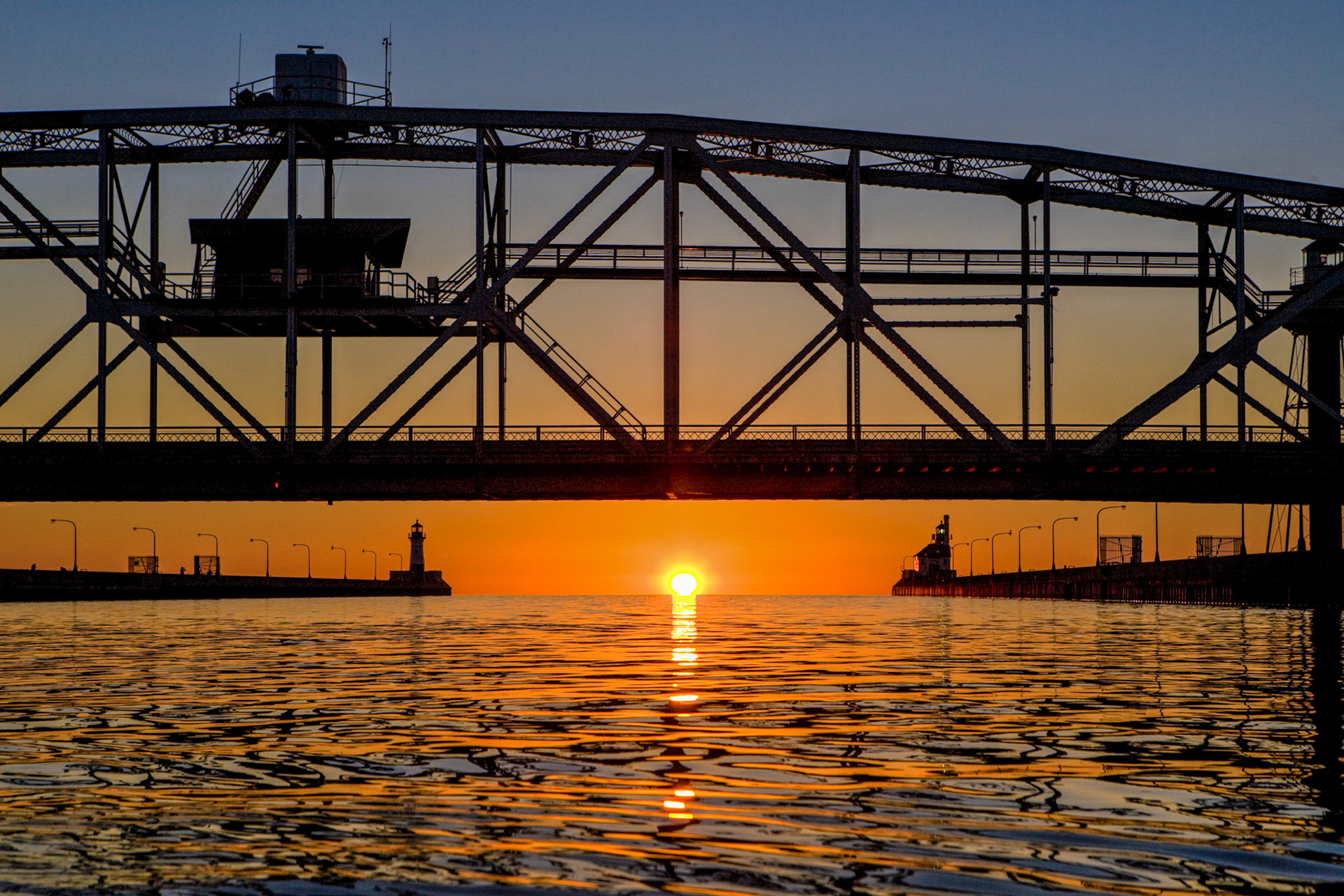 August 2—Down the Canal—Seeing a sunrise from a different perspective is always an exciting endeavor. This image, taken from a kayak, brings the light and water closer to our senses and envelopes us with the beauty of Lake Superior.Lake Superior's stunning blue hues and expansive horizon never fail to inspire awe and create a sense of tranquility.When you pass through the waters, I will be with you, and when you pass through the rivers, they will not sweep over you. When you walk through the fire, you will not be burned; the flames will not set you ablaze. Isaiah 43:2
