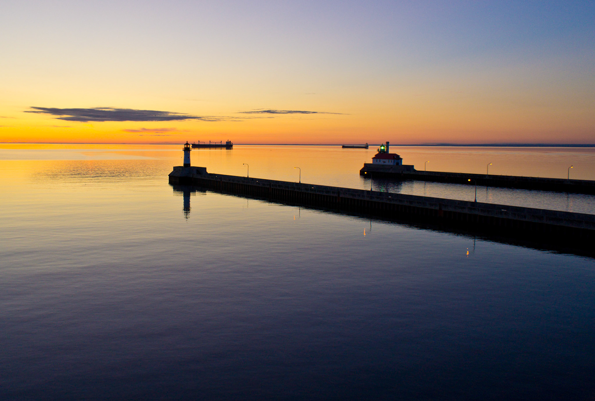 August 28—Calm Waters on Lake Superior—The light of a sunrise bathes the calm waters in warm beauty.“He made the storm be still and the waves of the sea were hushed. Then they were glad that the waters were quiet, and he brought them to their desired haven.” Psalm 107:29-30