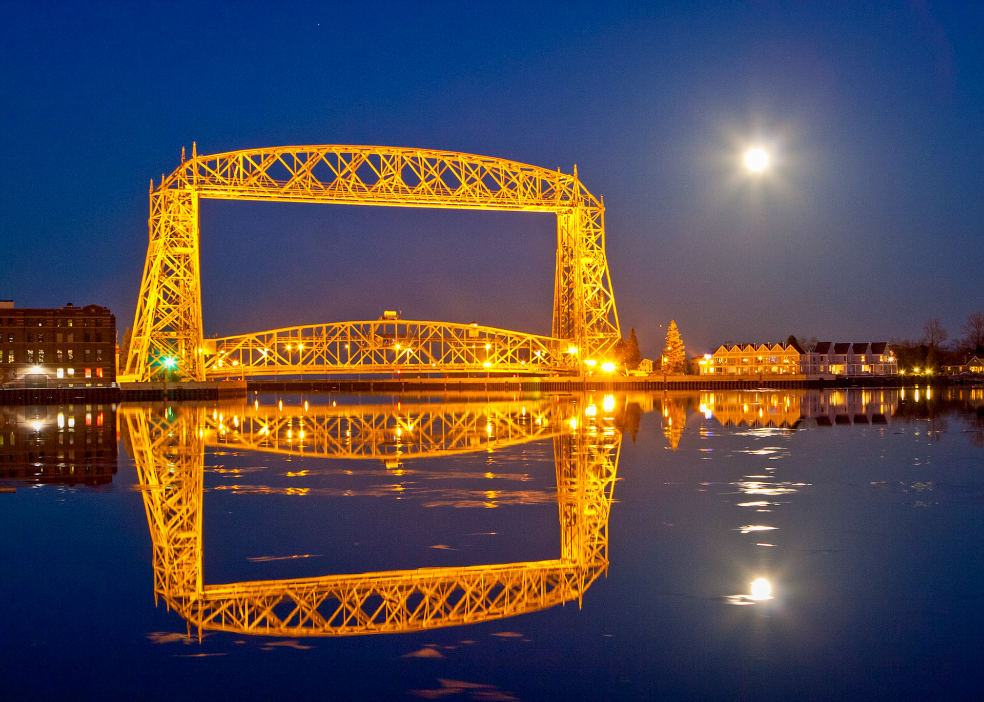 March 24 - Harbor ReflectionsOn a peaceful March evening, a full moon rises behind the lift bridge and casts its glow across the calm waters of Duluth Harbor. Even the faintest ripple can distort the image, turning a mirror into an abstract painting. Reflected light is also partially polarized — which is why a simple twist of a polarizing filter can either erase or intensify the mirrored sky.Reflections are interesting because they show an exact duplicate of the object being reflected, but they remain temporary and fleeting. They aren't real. A reflection appears only when the surface stays still.As in water, face reflects face, so the heart of man reflects the man. Proverbs 27:19 When life is unsettled, clarity fades. But in stillness, what is true becomes visible. Stillness reveals what chaos hides. When we quiet ourselves before the Lord, His image becomes clearer to us — Especially in the Word of God.