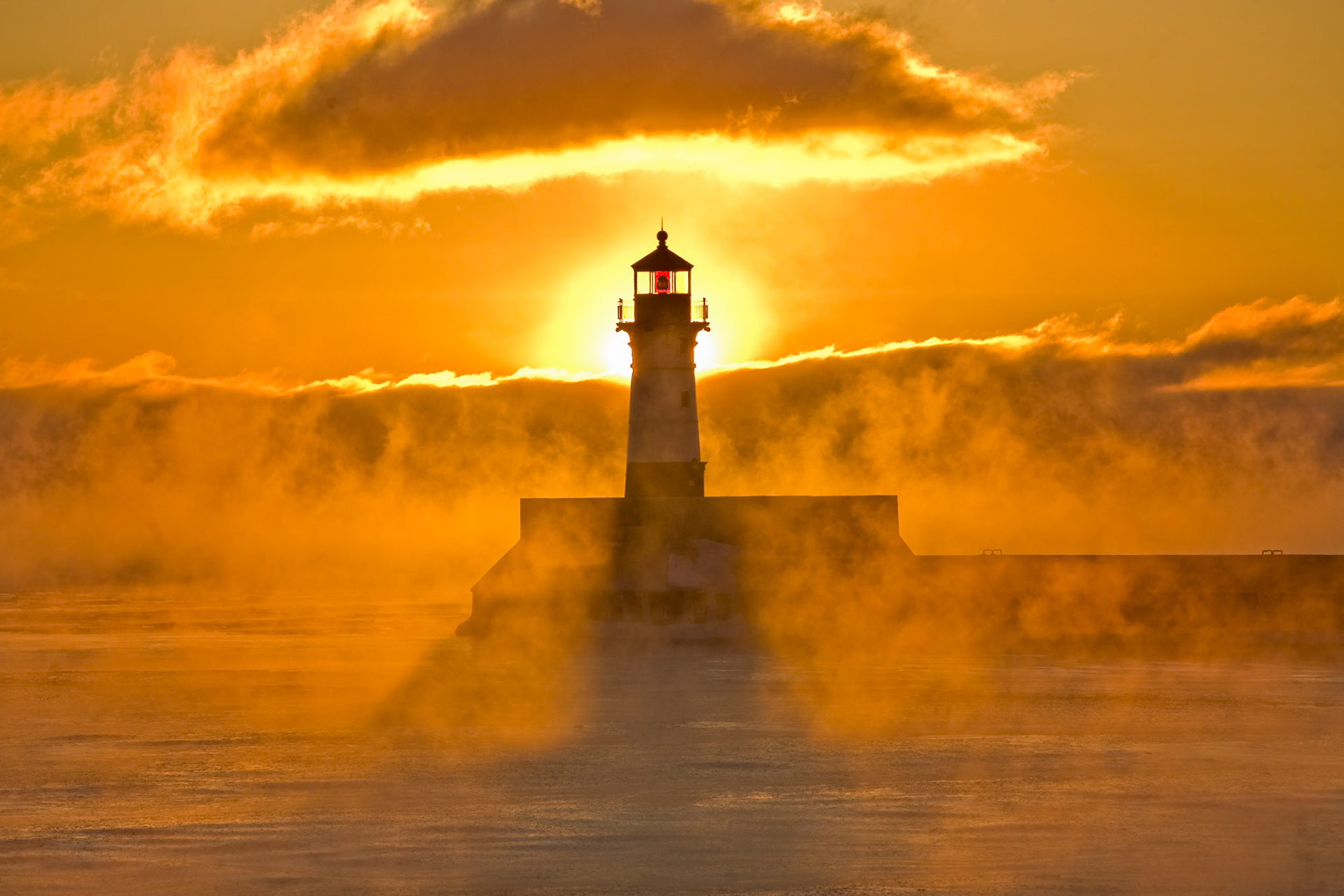 With open water on Lake Superior, this mornings bone chilling cold was sure to produce some interesting scenes along the lake shore.Mid-February and below zero temperatures are still hanging around. Although the strong Northwest winds dropped the wind chill into the -50F range, they pushed the lake ice off-shore exposing the relatively warm lake water to the frigid air. The 50 degree temperature difference between the water and the air created steam that lifted off the lake surface in waves of icy mist.As the sun made its way above the low lying clouds this morning, it beamed from behind the lighthouse and filled the sky with warm golden sunshine. Although the temperatures only rose to -10F as the day progress, the scene warmed the heart on a beautiful winter day along the shores of Lake Superior.God set the stars and planets into place to remind us of Him, what a privilege to be able to observe His creation.Psa 78:7 so that they might set their hope in God, and not forget the works of God