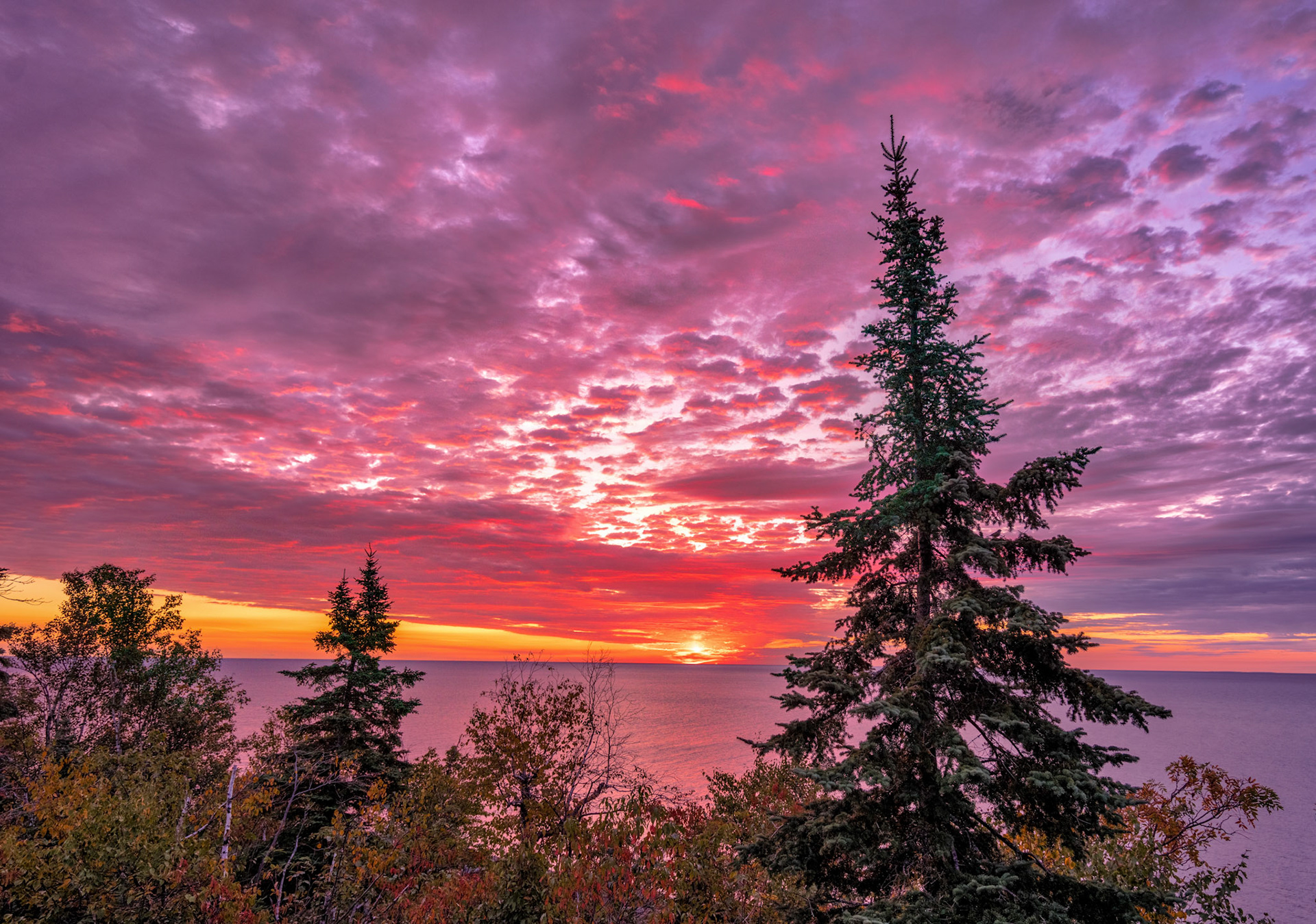 October 6—Daybreak at Palisade—The first light of morning breaks over Lake Superior as the clouds catch the light for a breathtaking display of God's created glory. Like the eyelids of creation opening to another day, the sun peeks over the horizon at precisely its appointed time.With the wide expanse of Lake Superior below and the immensity of the sky above, it's good to feel small in the hands of our creator.The Light of the WorldThis is the message we have heard from him and proclaim to you that God is light, and in him is no darkness at all. 1 John 1