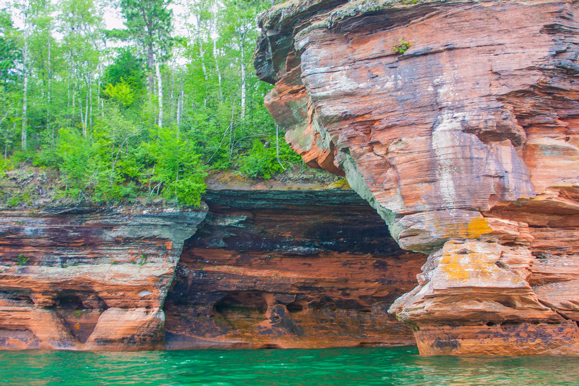 July 21—Sea Caves— Emerald Isles The sea caves offshore from the Bayfield Peninsula in Wisconsin have incredible sights and sounds. Accessible by kayak, the richly colored sandstone cliffs display the ages of erosion by the waves of Lake Superior. The deep, low eches of water in the inner chambers create a symphony of sound like no other on Earth.God is our refuge and strength, a very present help in trouble.Therefore will not we fear, though the Earth be removed, and though the mountains are carried into the midst of the sea;Though the waters roar and are troubled, the mountains shake with the swelling thereof. Selah. Psal  46:1