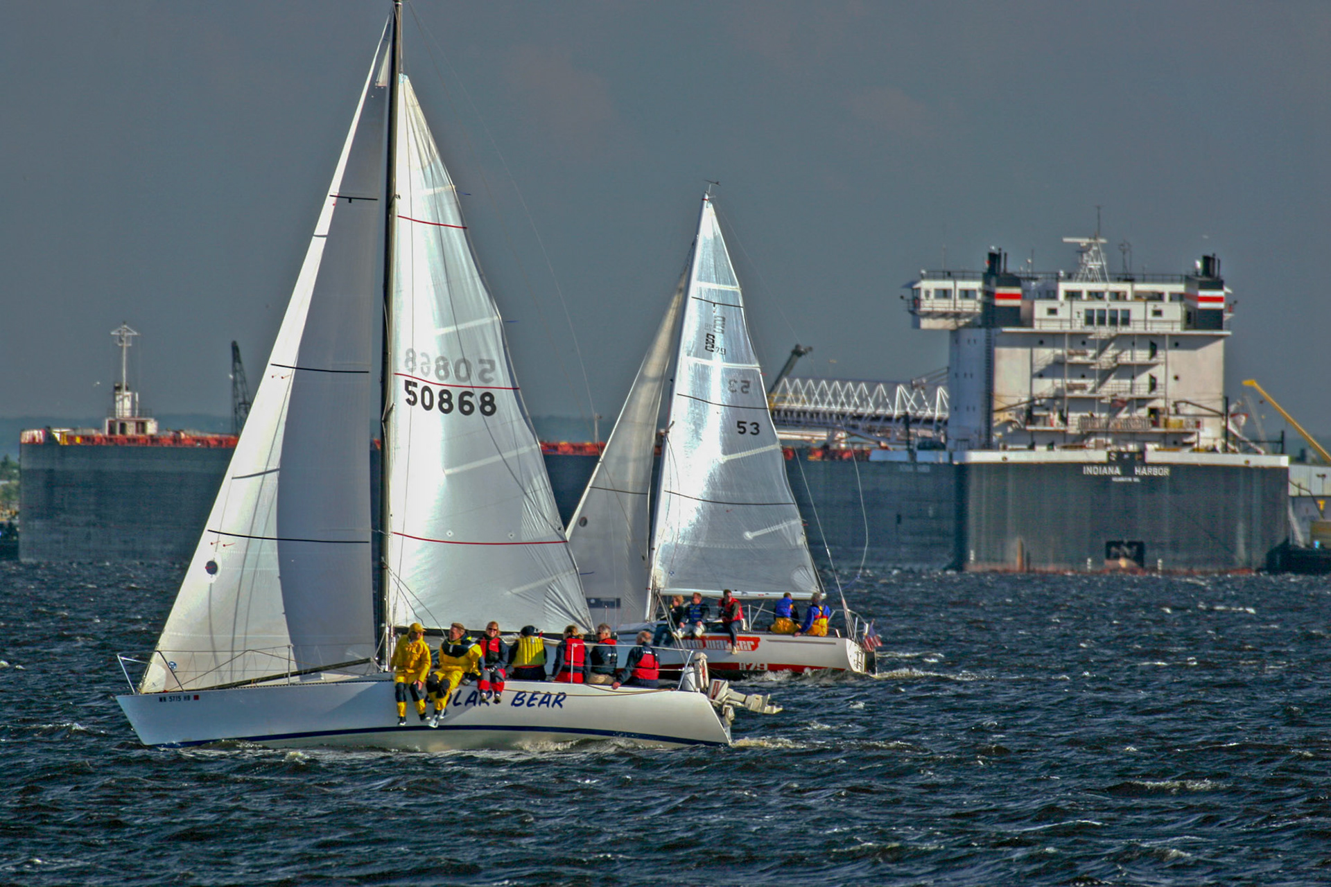 Wednesday night sailboat races in the Duluth Harbor are fun and challenging with 30 knot gusts and all hands on deck.Here, the 1000 ft Indiana Harbor waits to take on a load of coal, while sailboat enthusiasts enjoy an evening of boating.