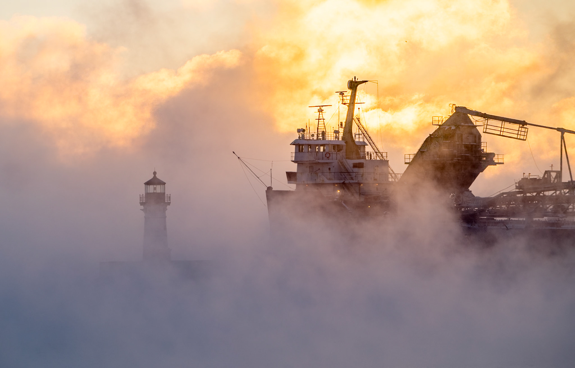 The Algolake departs Duluth on a frigid (-20F) December morning with the sun rising through the sea smoke to welcome the shiop back onto Lake Superior.