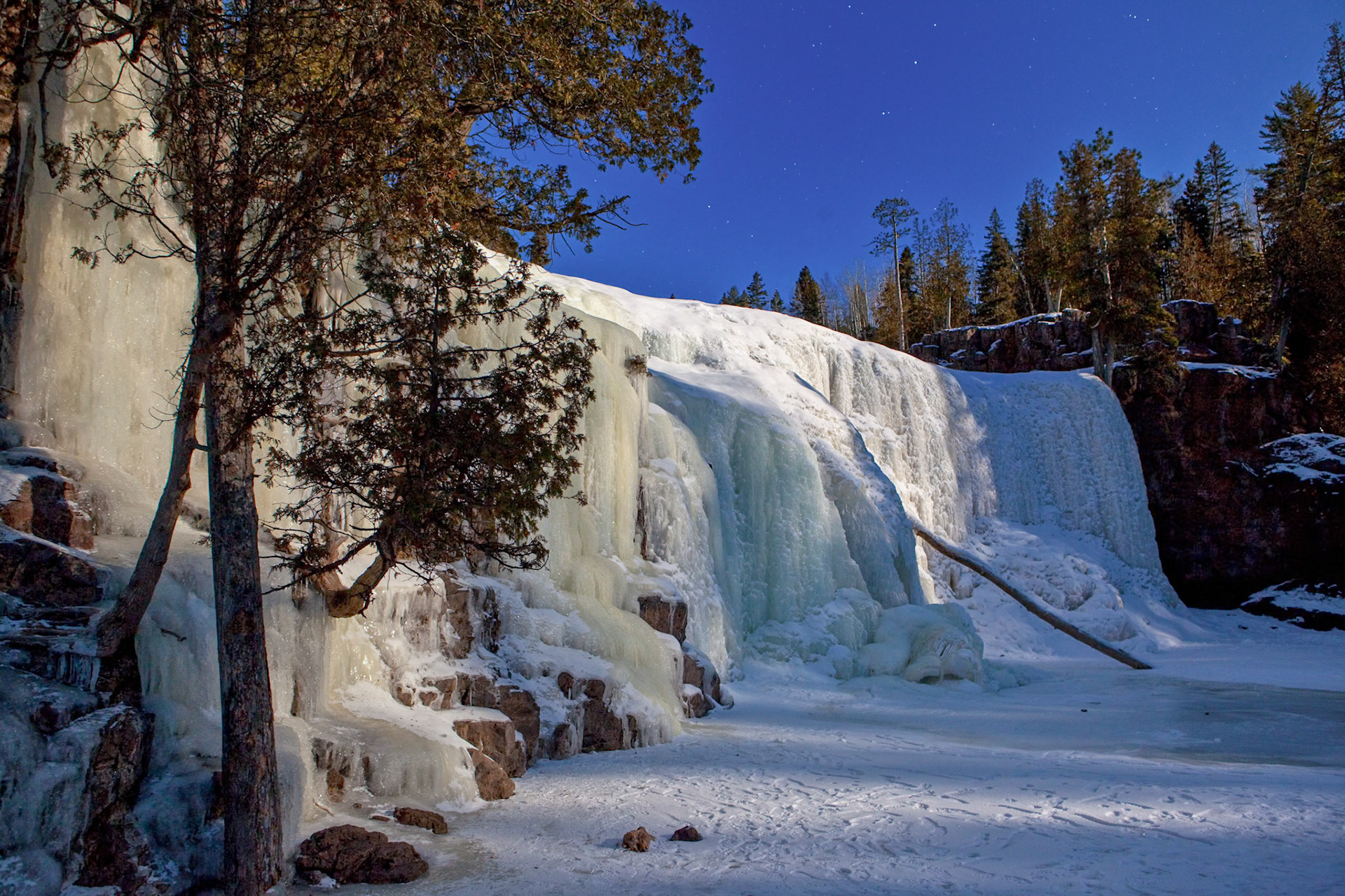 January 29 - Moonshine at Gooseberry FallsThe frozen waterfalls at Gooseberry Falls State Park look much different when bathed in the moonlight of a full January moon.On a cold, clear January night with fresh snow on the ground, moonlight can feel dramatically brighter than usual — even though it's still hundreds of thousands of times dimmer than daylight. Fresh snow reflects up to 90% of incoming light, acting like a giant mirror, and the camera sensor, with a slow shutter speed, easily captures this light into interesting imagery.The evening's quiet is broken only by an occasional owl hoot and the muted bubbling of the Gooseberry River, which is still moving under the ice and snow.He reveals deep and hidden things;He knows what lies in darkness,and light dwells with him. Daniel 2:22What you see when you walk outside under the light of a full moon is incredible. What you see under the light of the Gospel far outshines anything else.