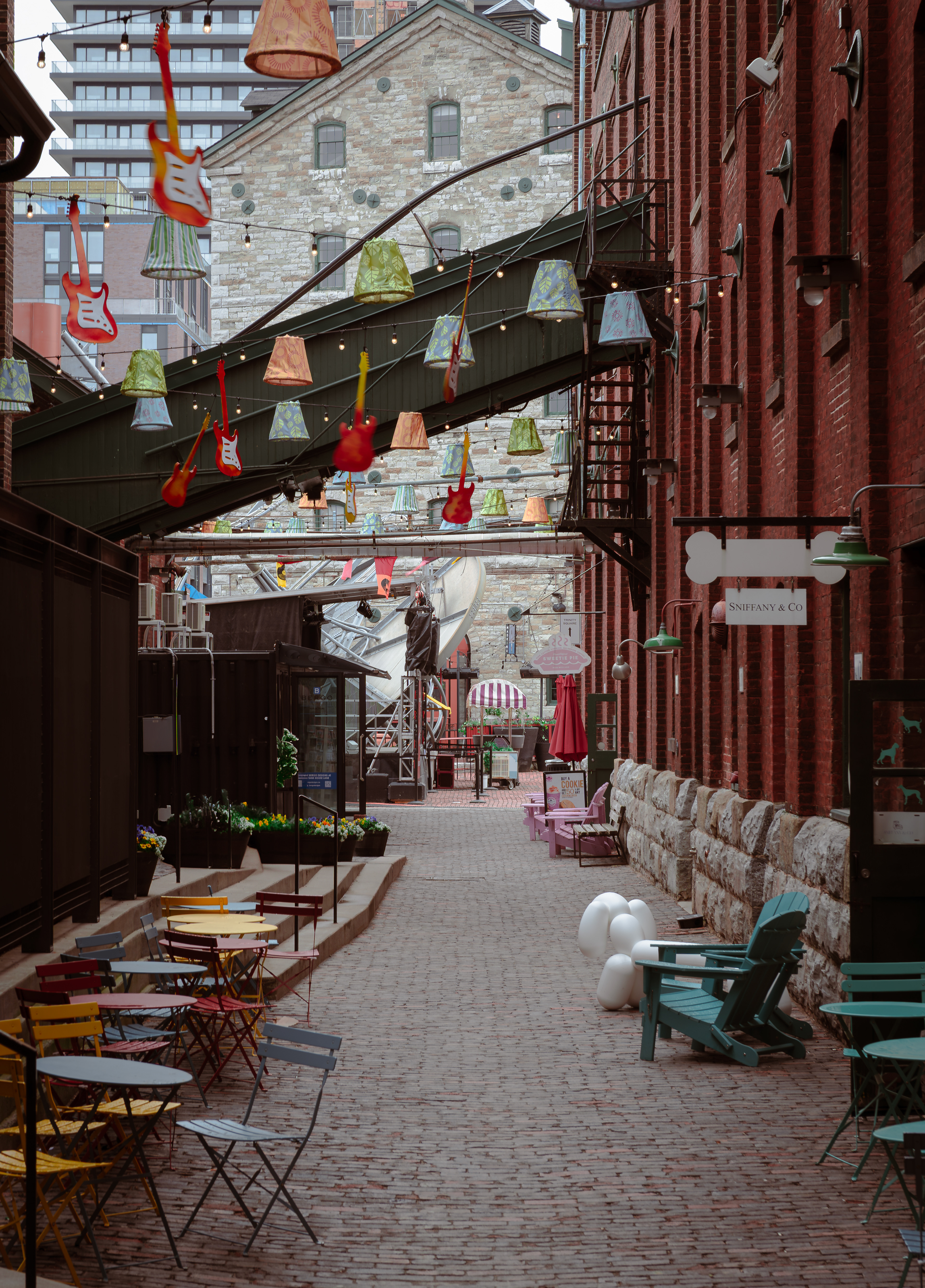 Colorful alley in Toronto’s Distillery District lined with vintage brick, patio chairs, and overhead hanging guitars.