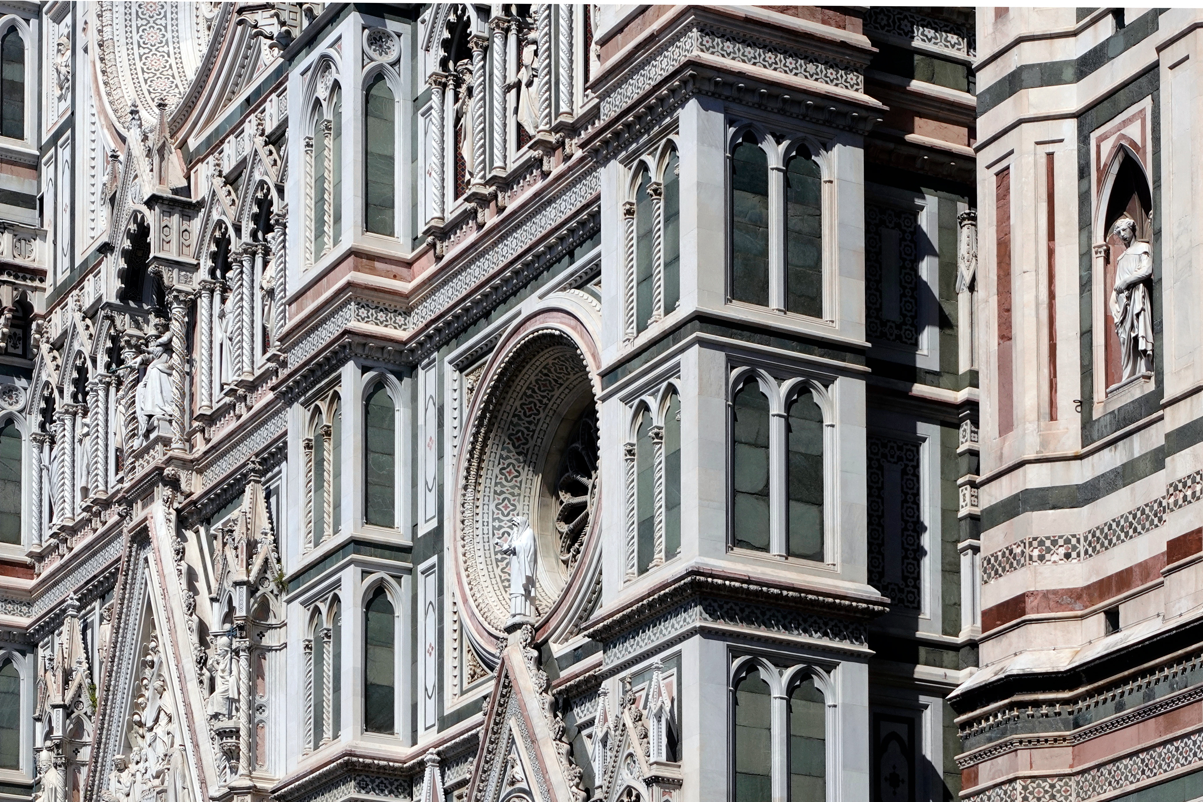  The exterior of the Duomo, formally the Cathedral of Saint Mary of the Flower, in Florence is faced with polychrome marble panels in various shades of green and pink, bordered by white.
