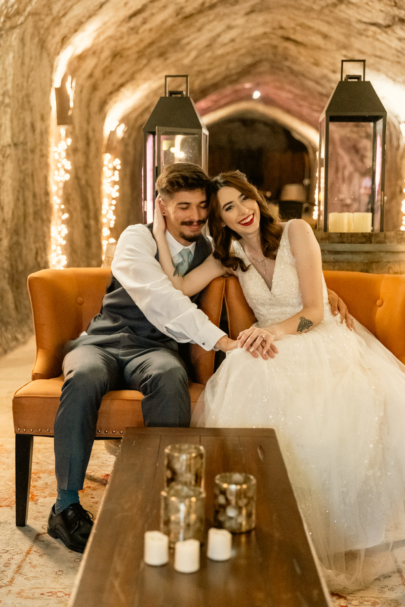 groom-and-bride-sit-na-wine-cave-lighted-by-tiny-string-lights