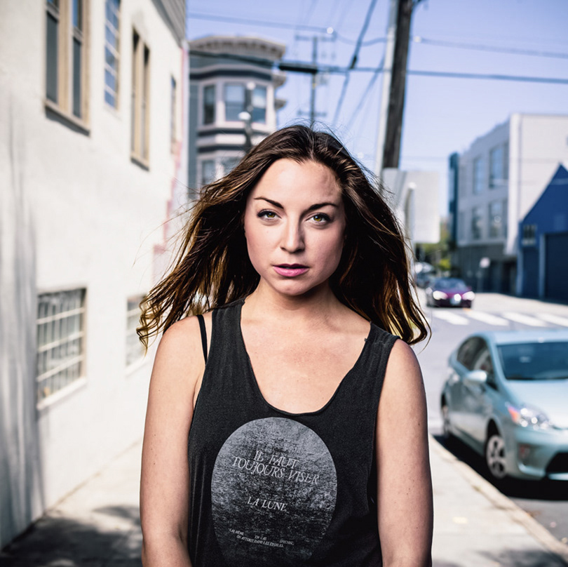 Young-woman-with-medium-length-straight-brown-hair-wears-a-black-tank-top-and-walks-up-a-san-francisco-sidewalk