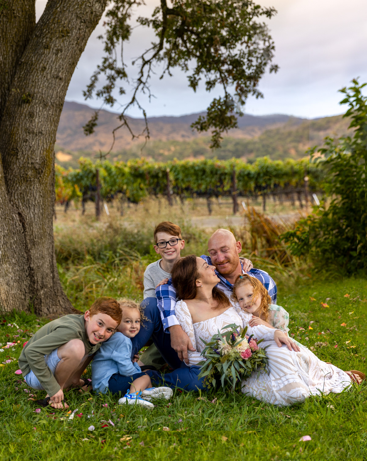 parents-four-children-sit-on-grass-under-tree-in-Napa-Valley-vineyard-park