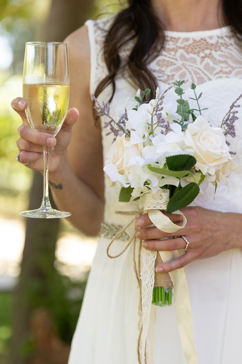 bride-holds-a-glass-of-champagne-in-one-hand-and-a-white-rose-bouquet-in-a-ringed-hand