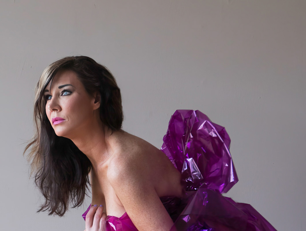 woman-with-blue-eyes-long-brown-hair-looks-to-the-side-and-is-wrapped-in-pink-cellophane-dress