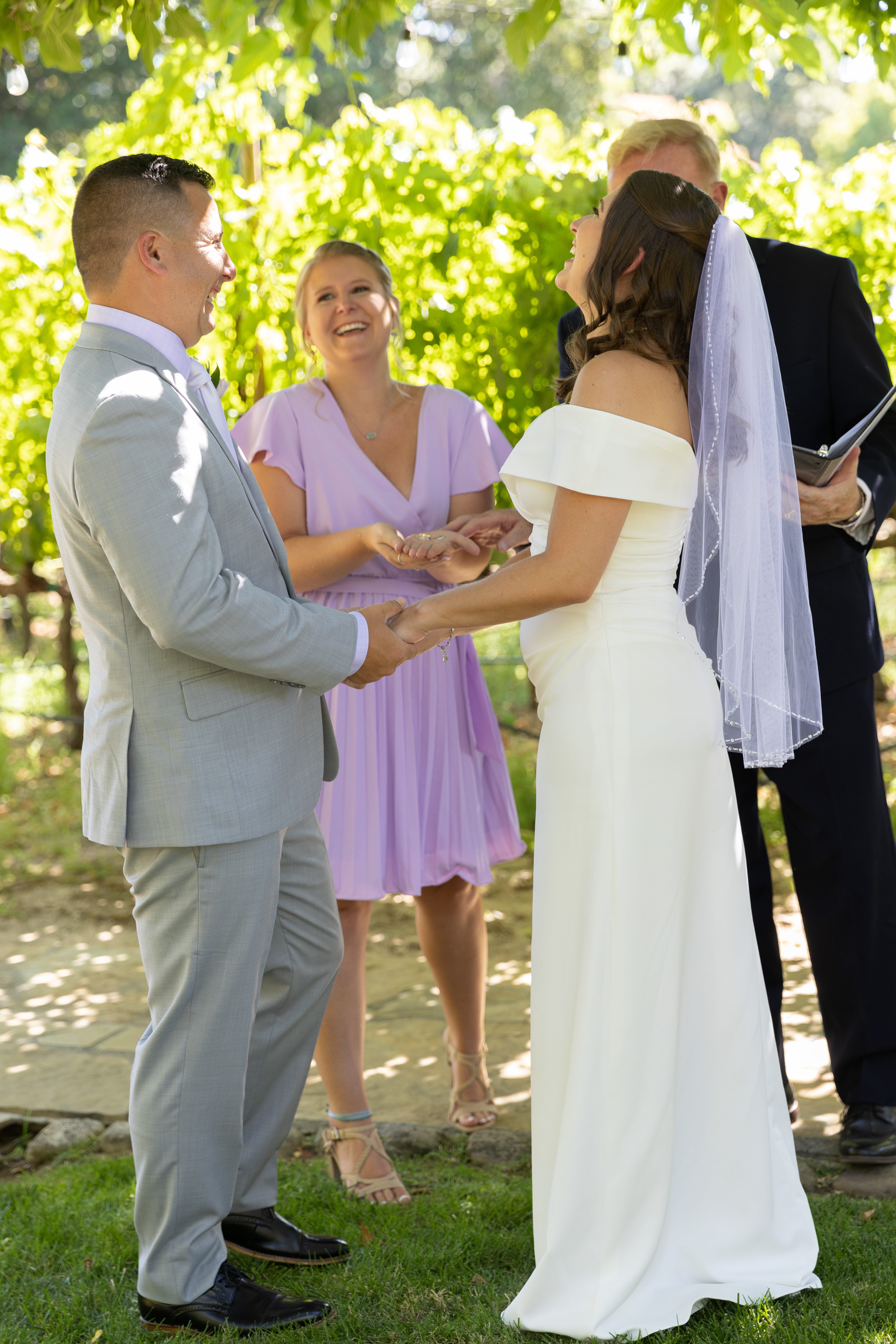 Bride-groom-and-made-0f-honor-hold-hands-laughing-in-napa-vineyard