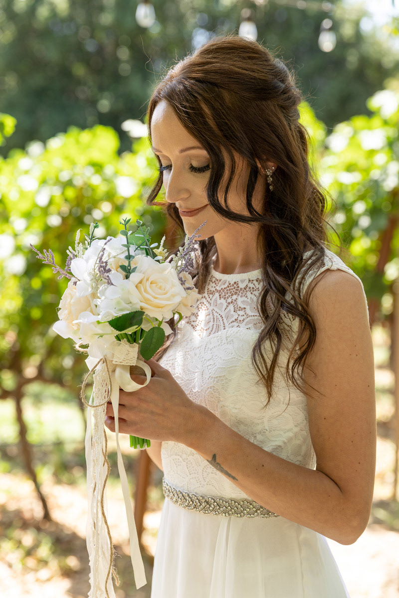 Set-among-a-Napa-Vineyard-a-bride-with-long-curled-brown-hair-smelling-a-white-rose-bouquet