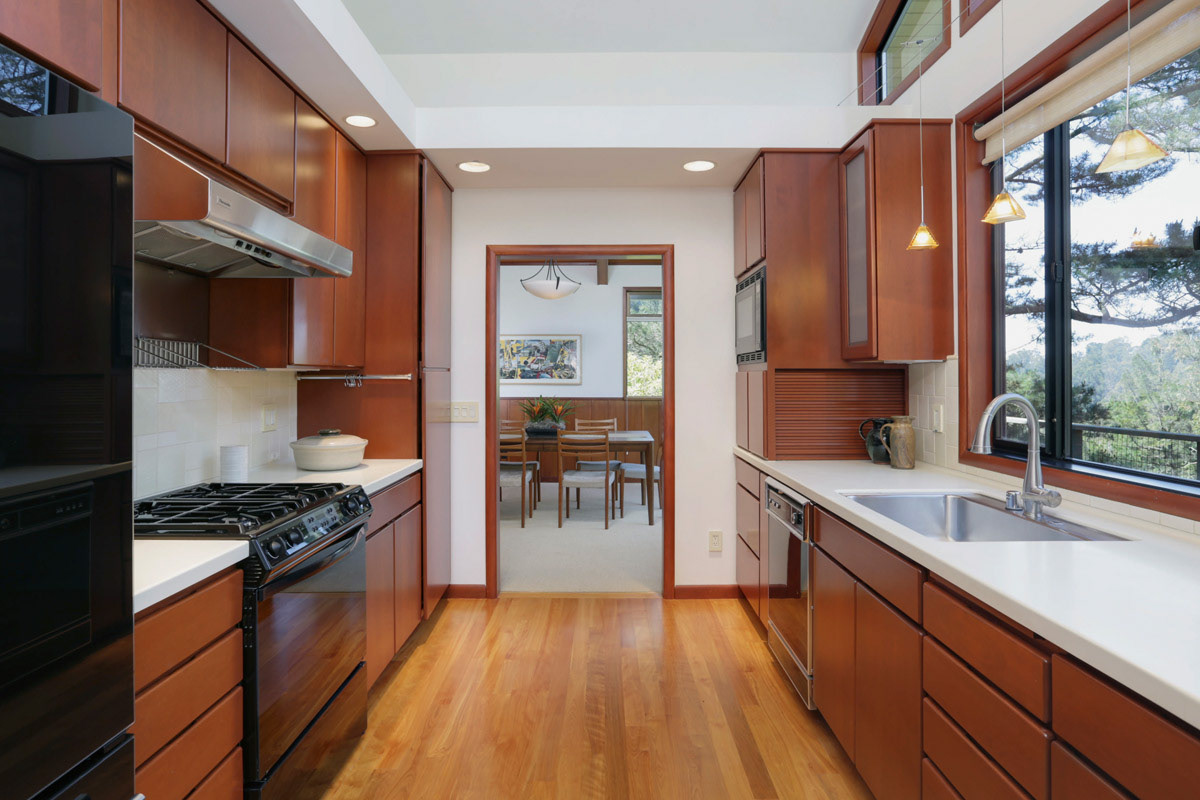 galley-kitchen-cherry-stained-cabinets-white-quartz-counters-doorway-to-dining-room
