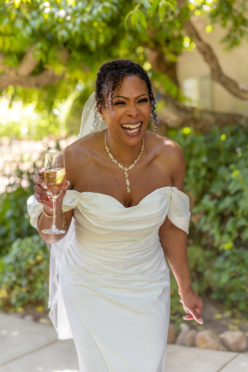 a-bride-laughs-half-bent-forward-while-holding-a-glass-of-champagne-in-a-Napa-Valley-Vineyard