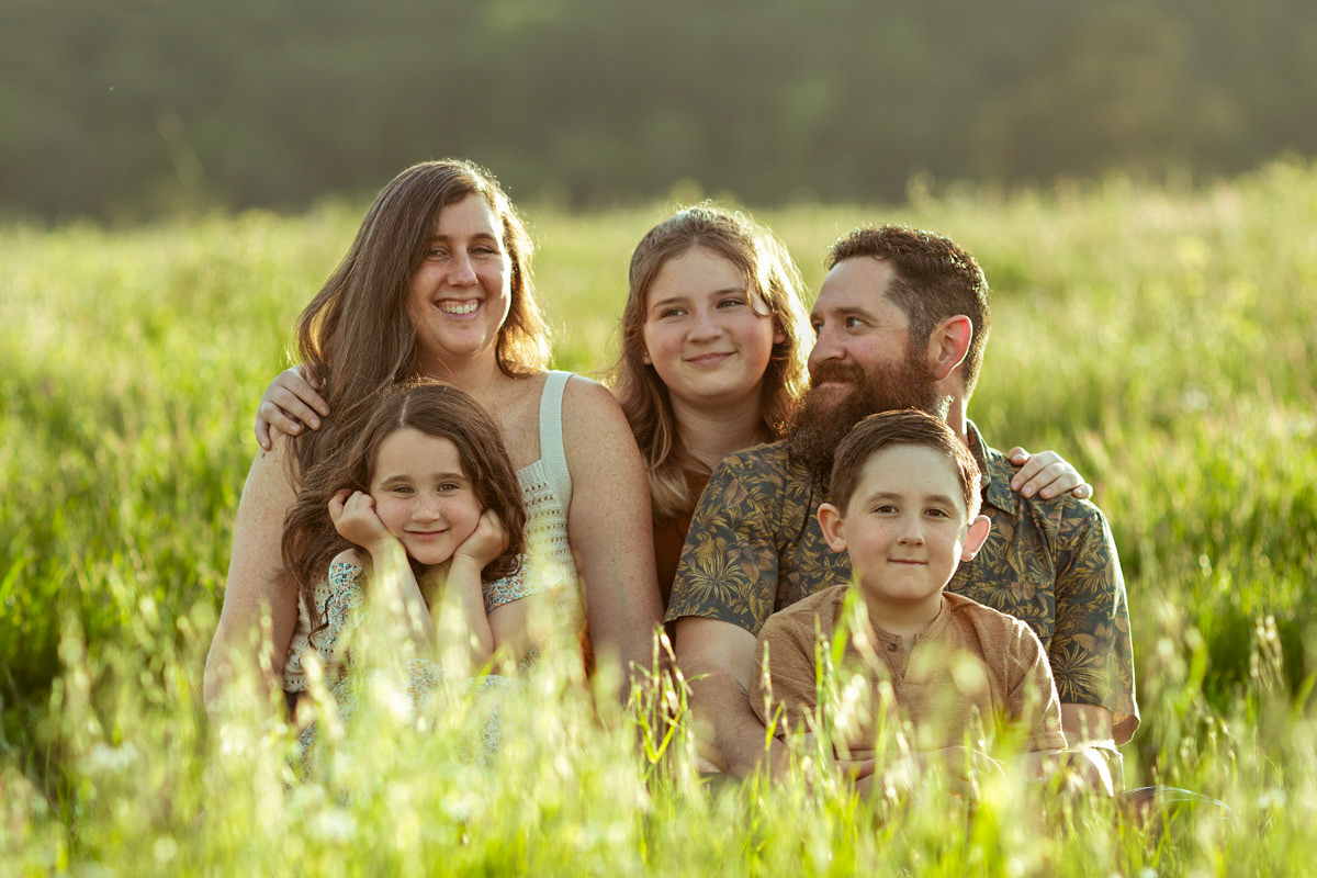 family-of-five-sit-in-field-half-hidden-by-tall-grass