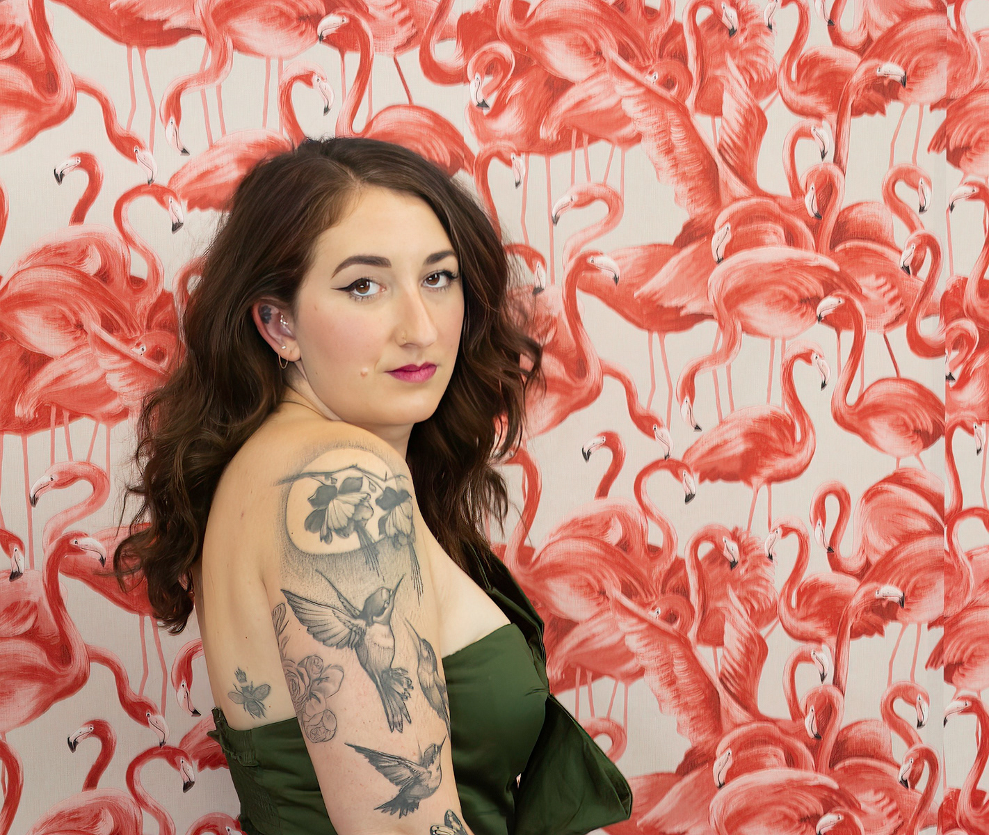 Young-woman-with-long-wavy-brown-hair-manicured-eyebrows-pink-lipstick-looks-out-over-her-tattooed-shoulder