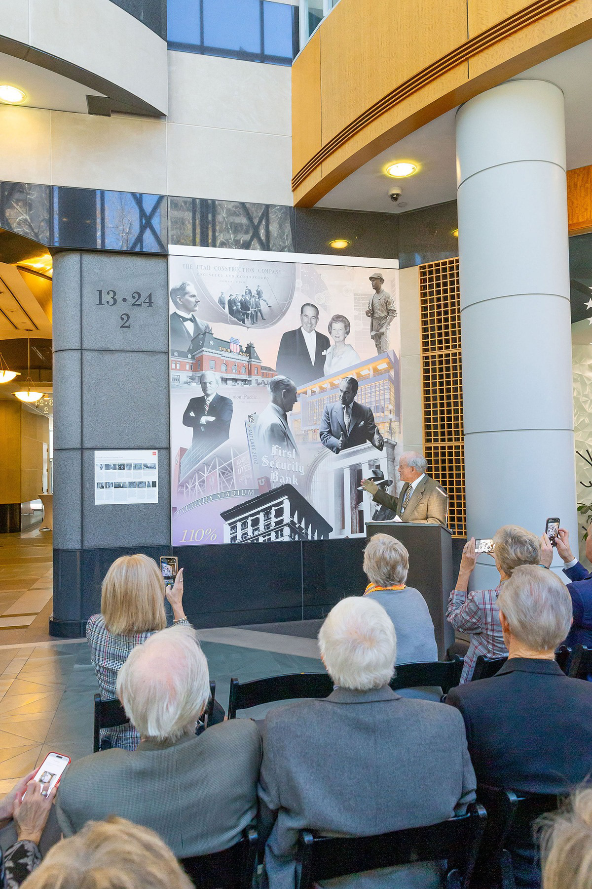 Eccles and First Security Heritage Mural and companion archival image key installed between columns in the Wells Fargo Center lobby, with attendees at the unveiling.