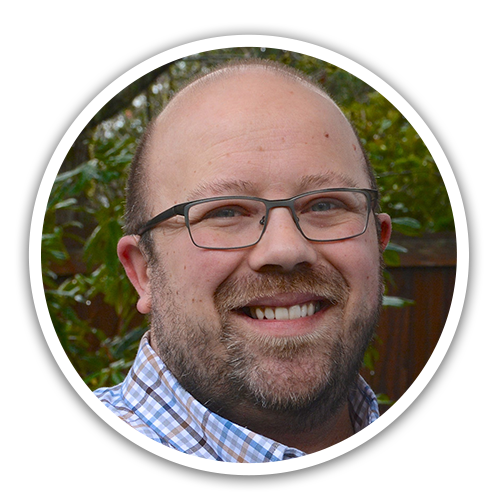 Photo of Lee Thompson, a caucasian male with a beard, short cut hair (balding) with glasses, wearing a light colored plaid shirt.