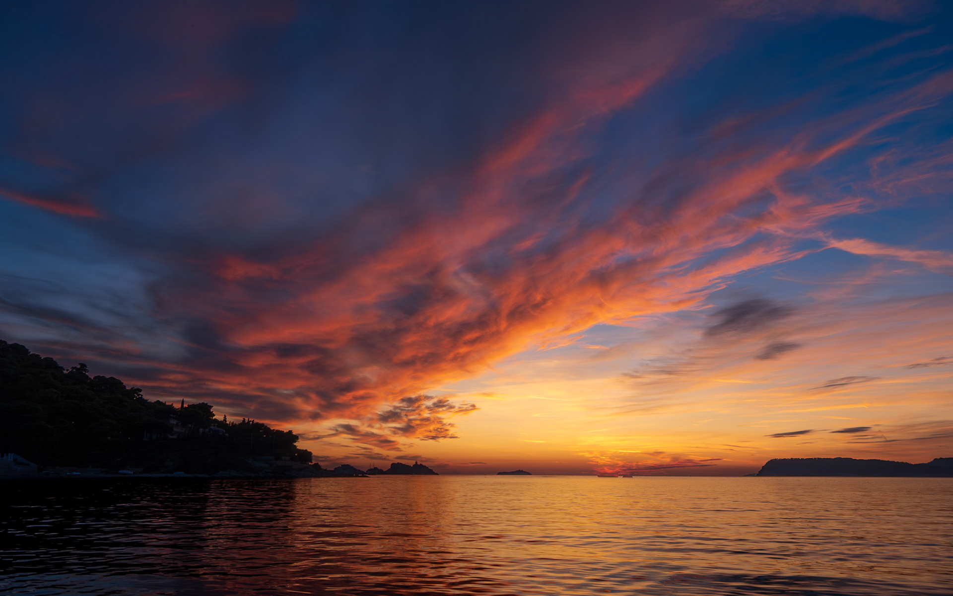 Intense reds and oranges stretch across the Croatian sky at sunset, mirrored in the placid water below.