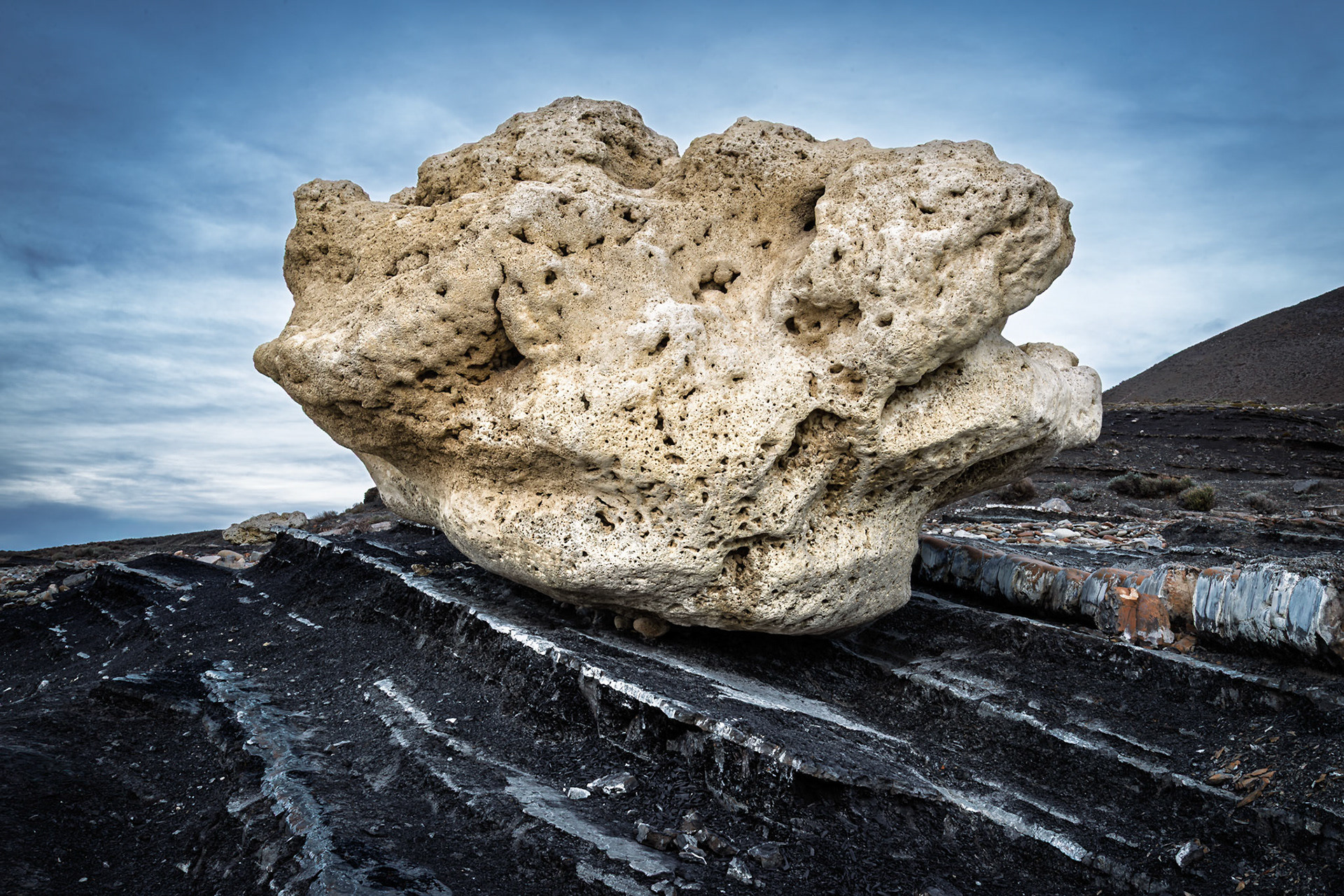 A fantastical, porous boulder resembling ancient coral lies perched atop striped volcanic slabs, sculpted by time in Torres del Paine.