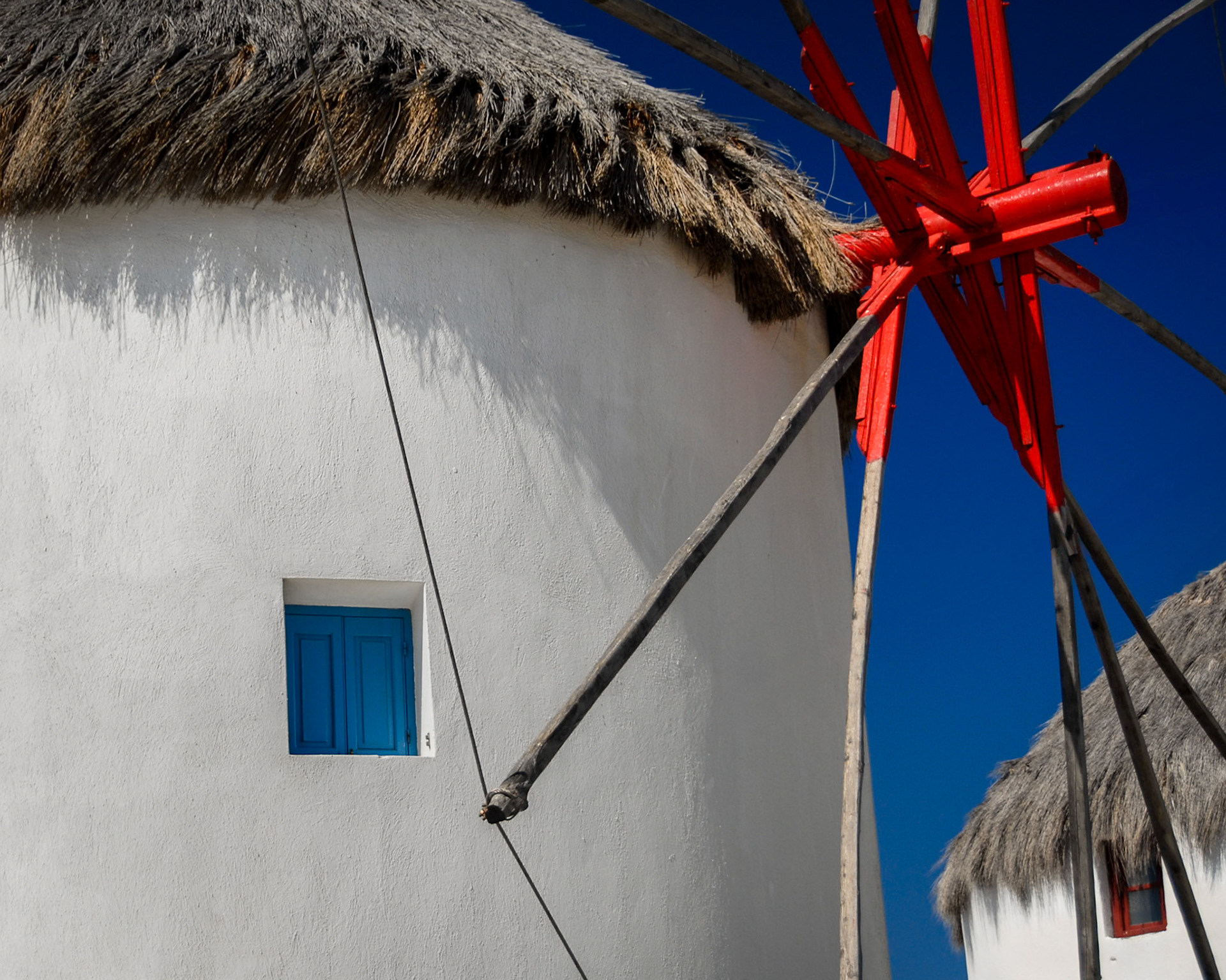 Classic Cycladic windmill framed by thatched roofing and red-painted beams.