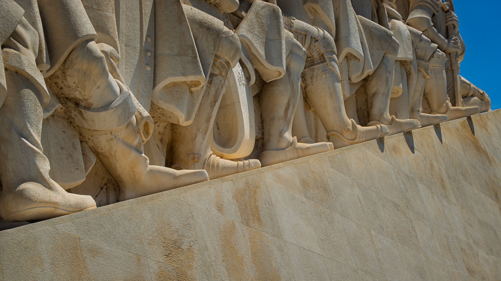 Boots and robes of explorers emerge from stone, midstride in a sculpted procession at Lisbon’s Monument of Discovery.