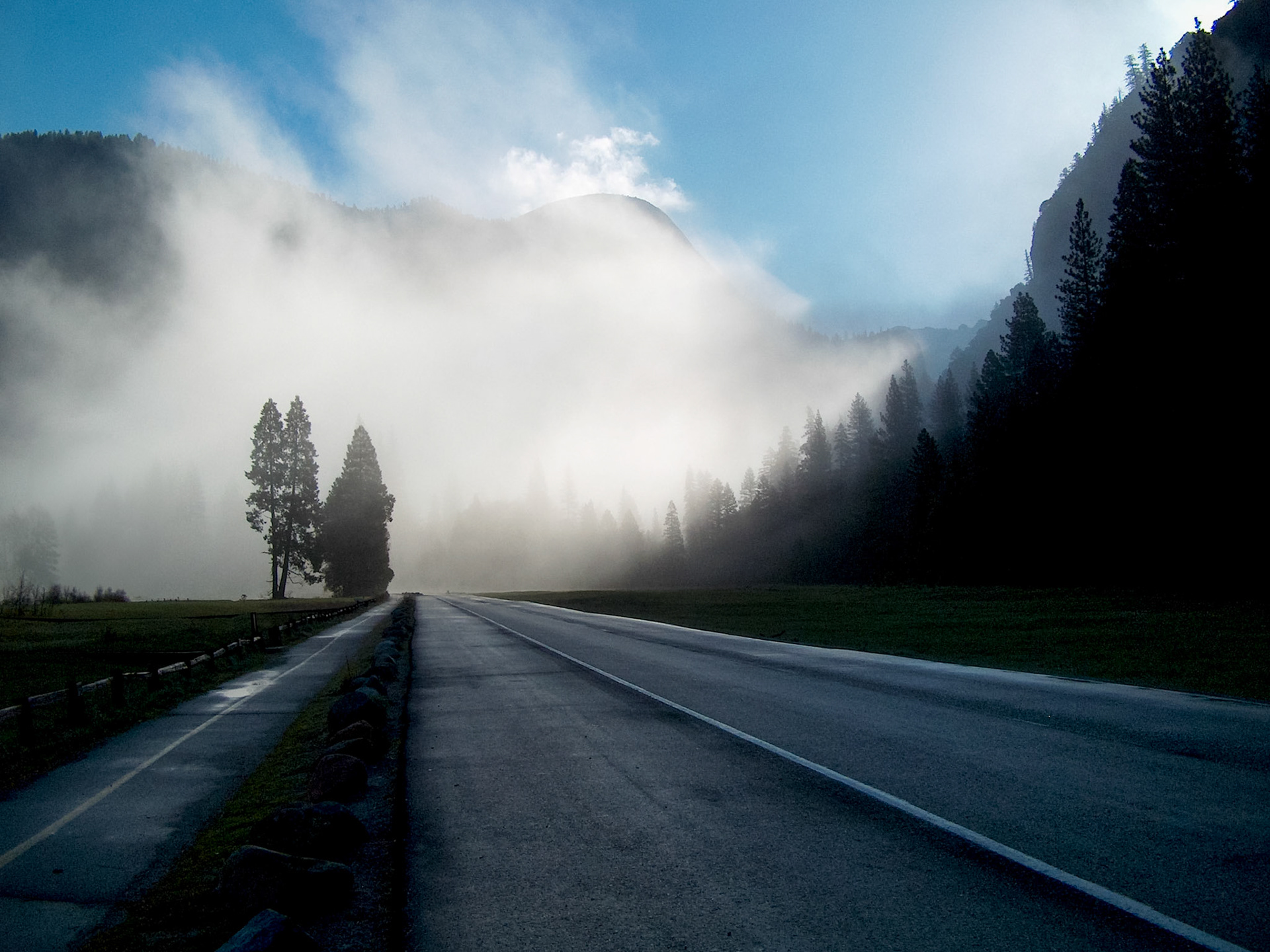 A Yosemite road cuts through an open valley with fog shrouding the scene ahead.
