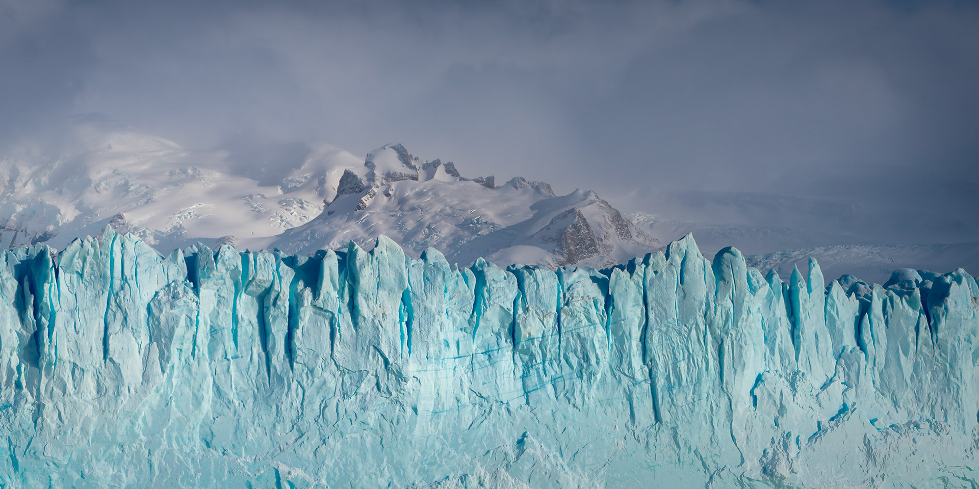 Glacial ice rises in jagged symmetry beneath a booding sky.