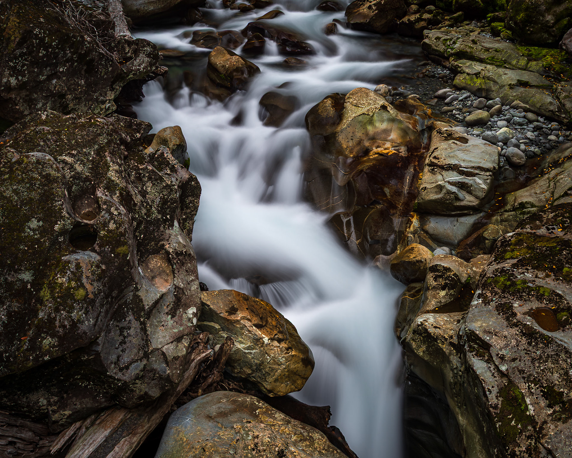 A cascade of glacier-fed water rushes through weathered rock, deep in a South Island gorge.