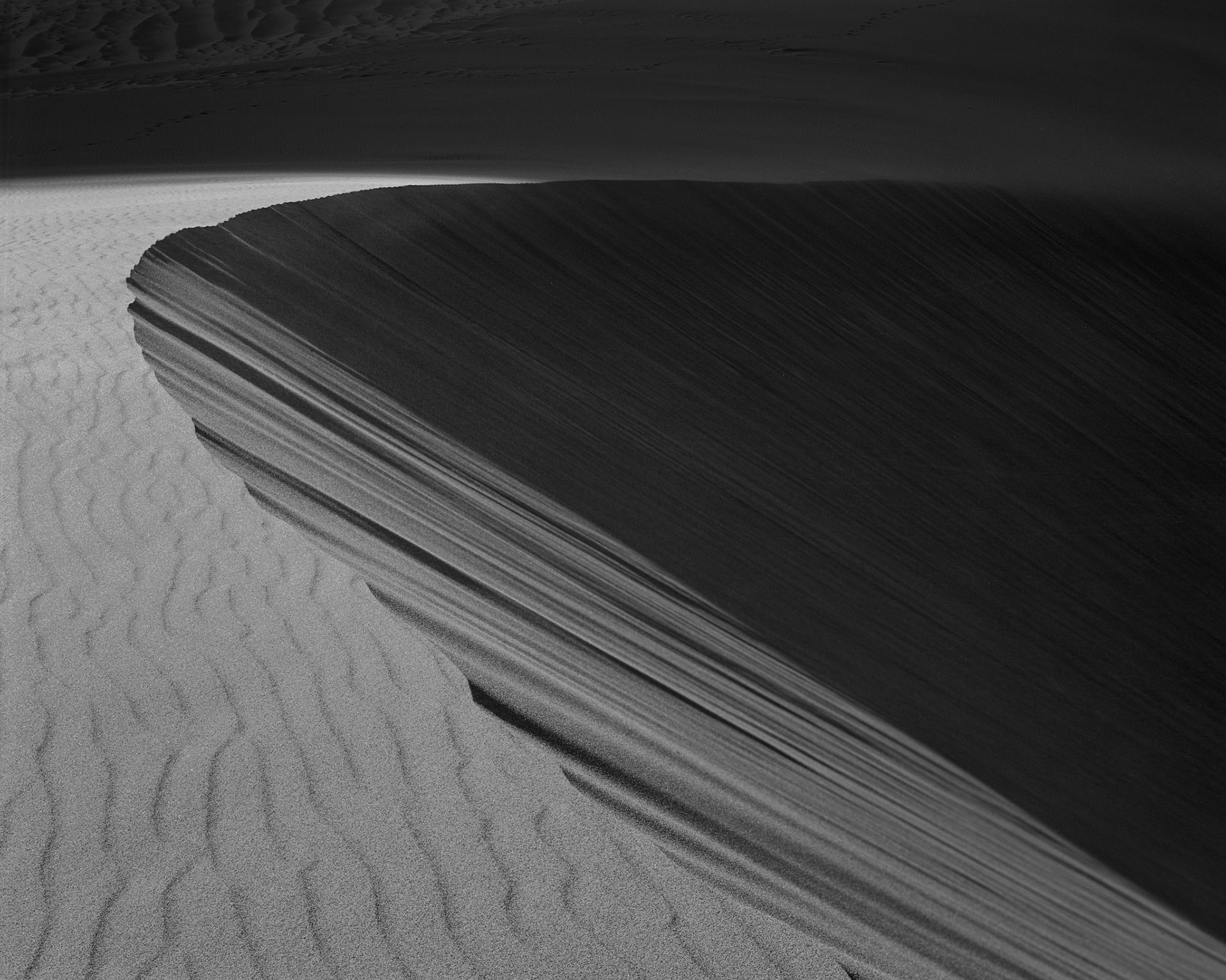 A sweeping shadow curves along a dune edge in Great Sand Dunes National Park.
