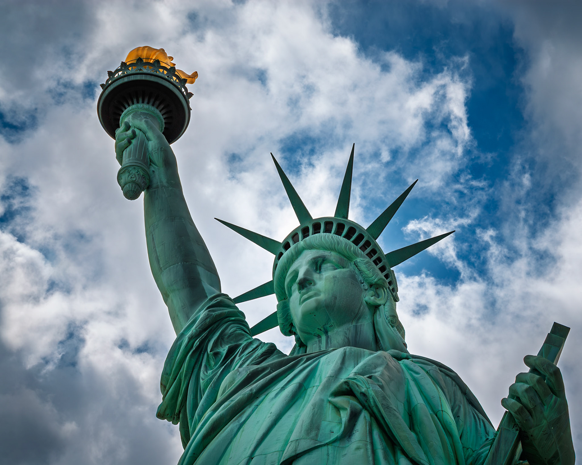 Lady LIberty's torch pierces the clouds as a beacon of hope.
