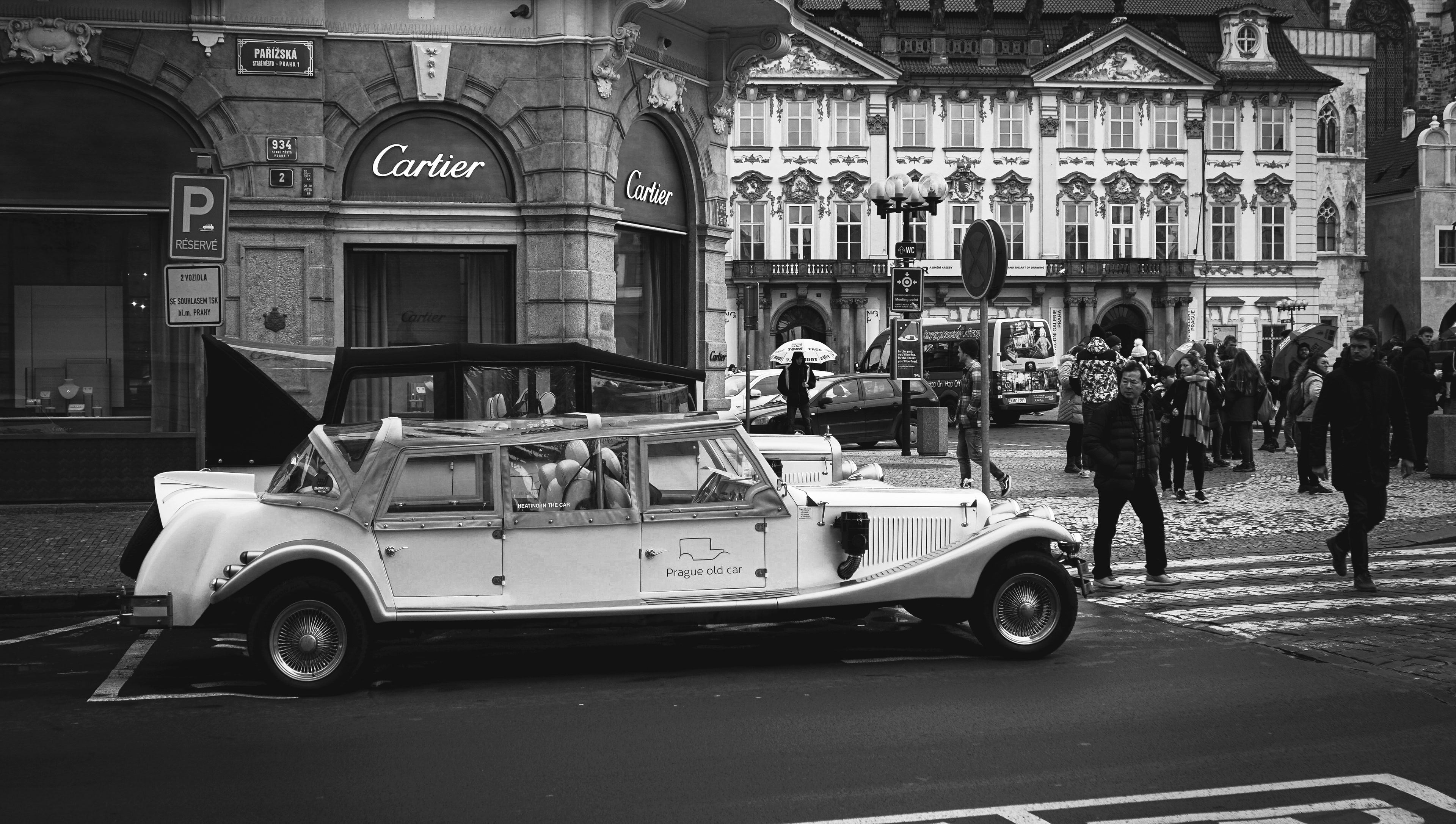 Street Photography. This image was taken in Prague city centre. Black and white city photography portrays the old times and nowadays. In the photograph there is a vintage car: Prague old cars and in the second plan there are people wearing modern clothes. 