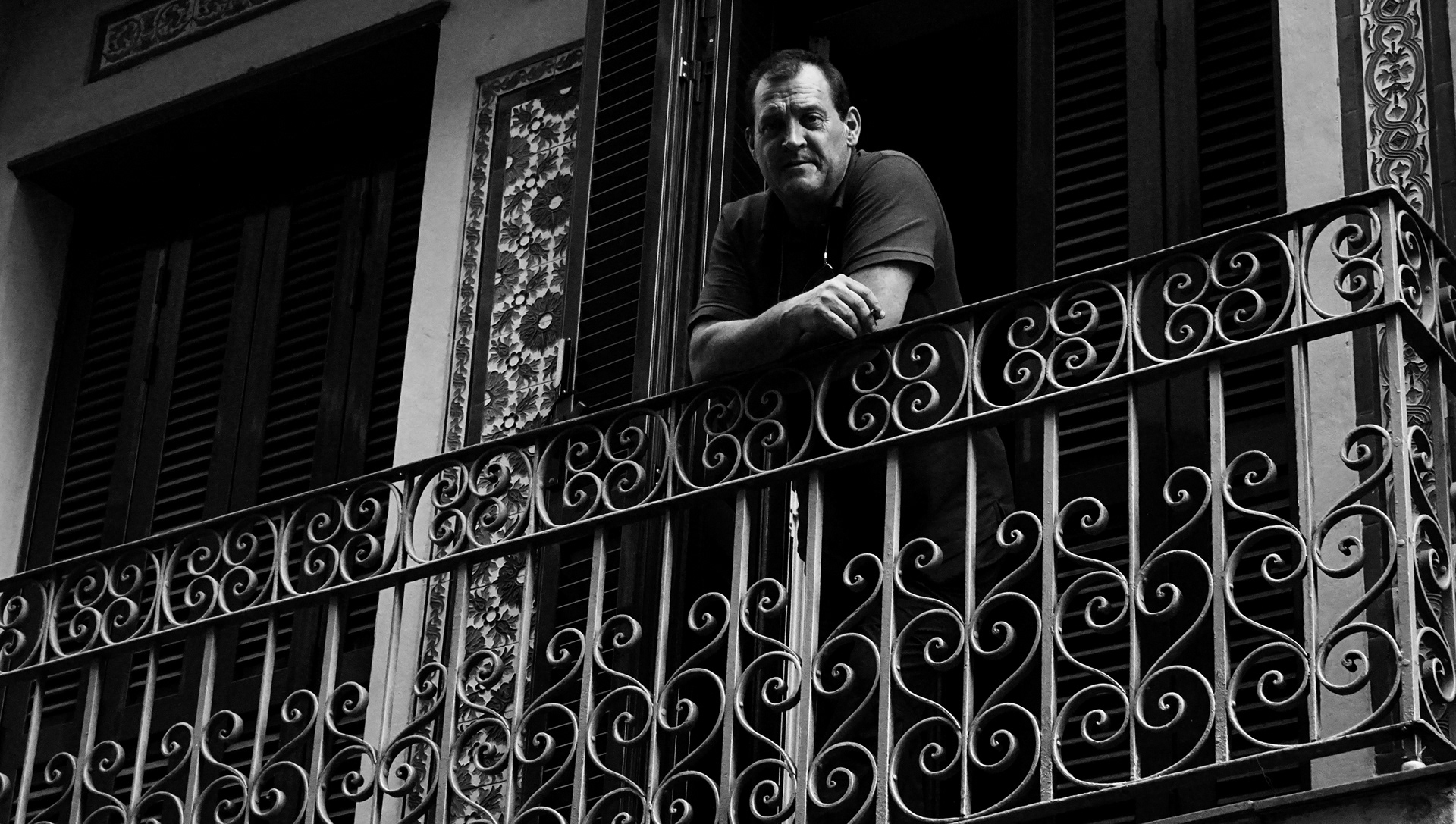 Black and white documentary photography of a man smoking in the balcony in the middle of small Spanish village. Photography of an emotion