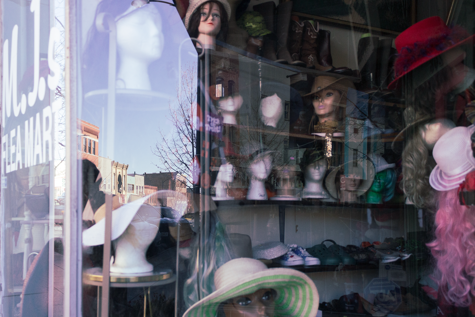 Shelves of mannequin heads with eccentric hats sit behind a window.