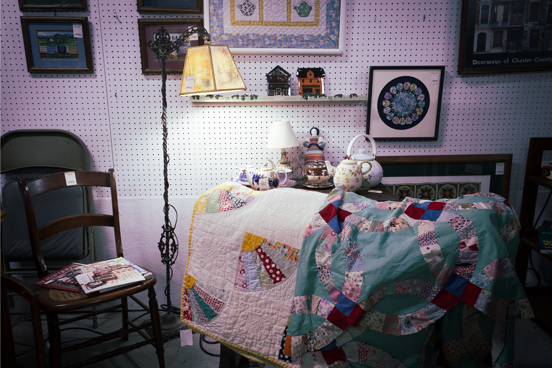 A lamp illuminates quilts and other items on sale in a flea market booth.