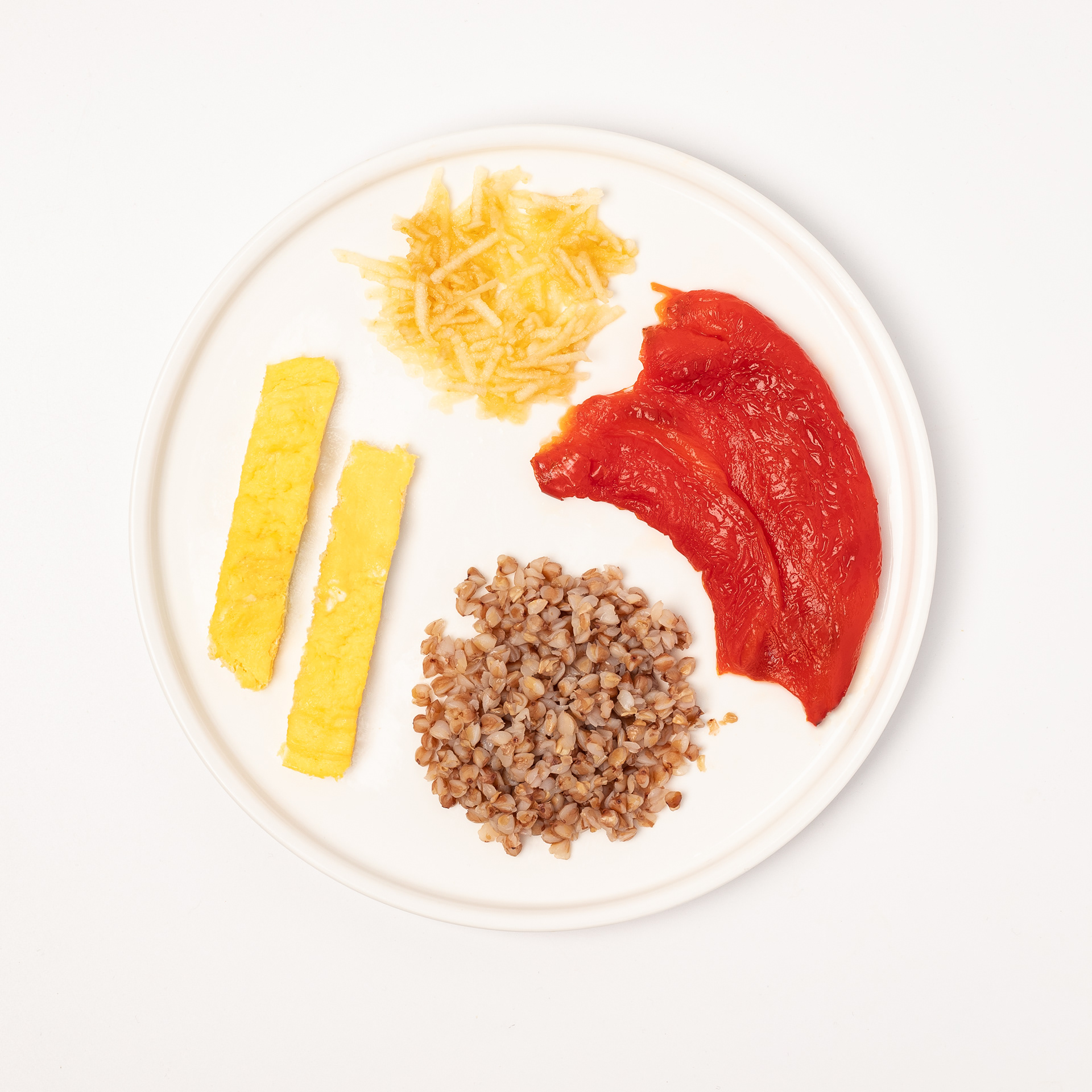 Top view of a baby food plate with buckwheat, scrambled egg strips, grated apple, and cooked red pepper. Food photography by Uliana Kopanytcia for a baby nutrition app