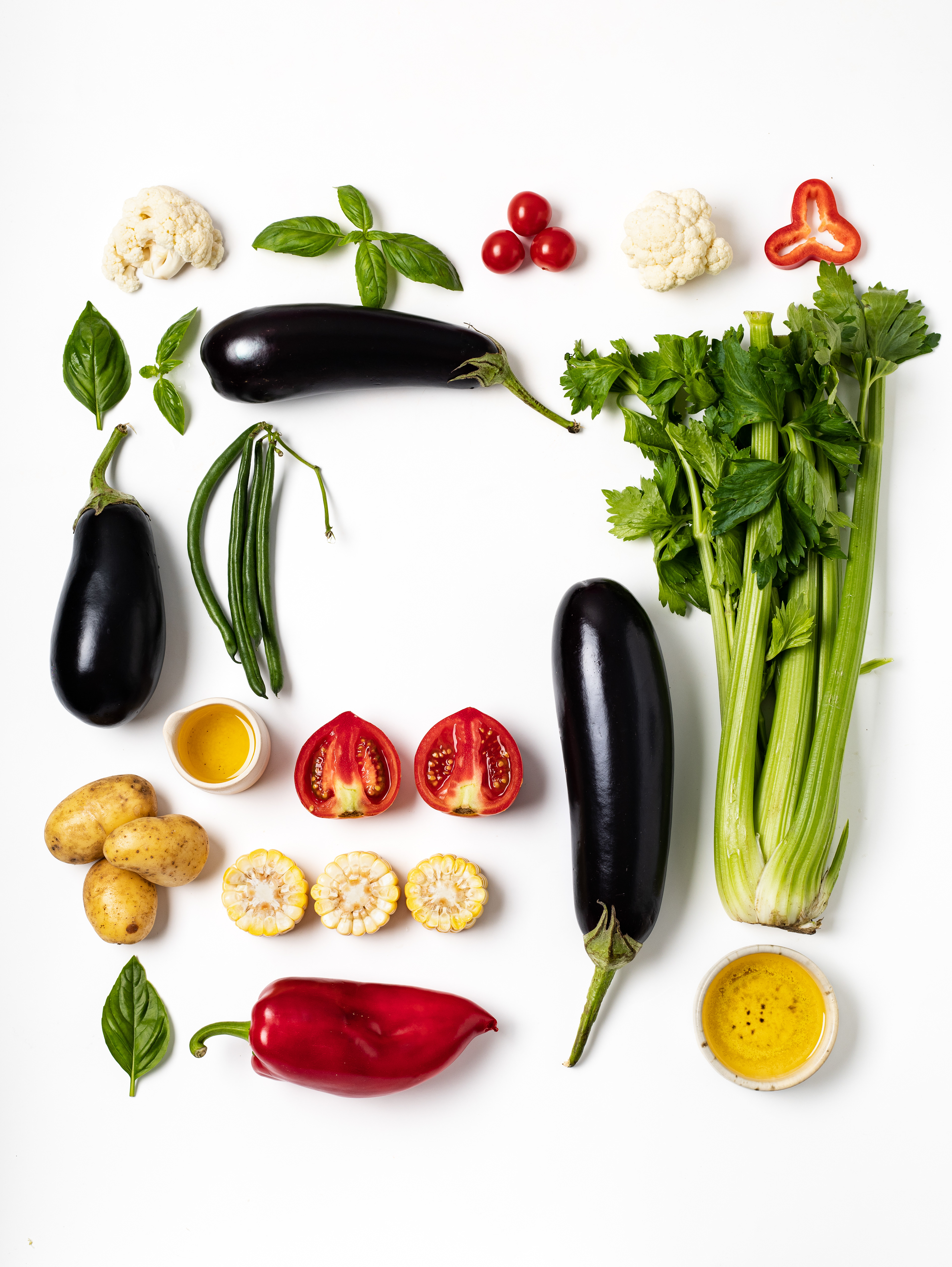 Assorted vegetables arranged on a white background: eggplants, green beans, celery, tomatoes, corn, red bell pepper, basil, cauliflower, potatoes, and dipping sauces. Food photography by Uliana Kopanytcia for a children's nutrition app