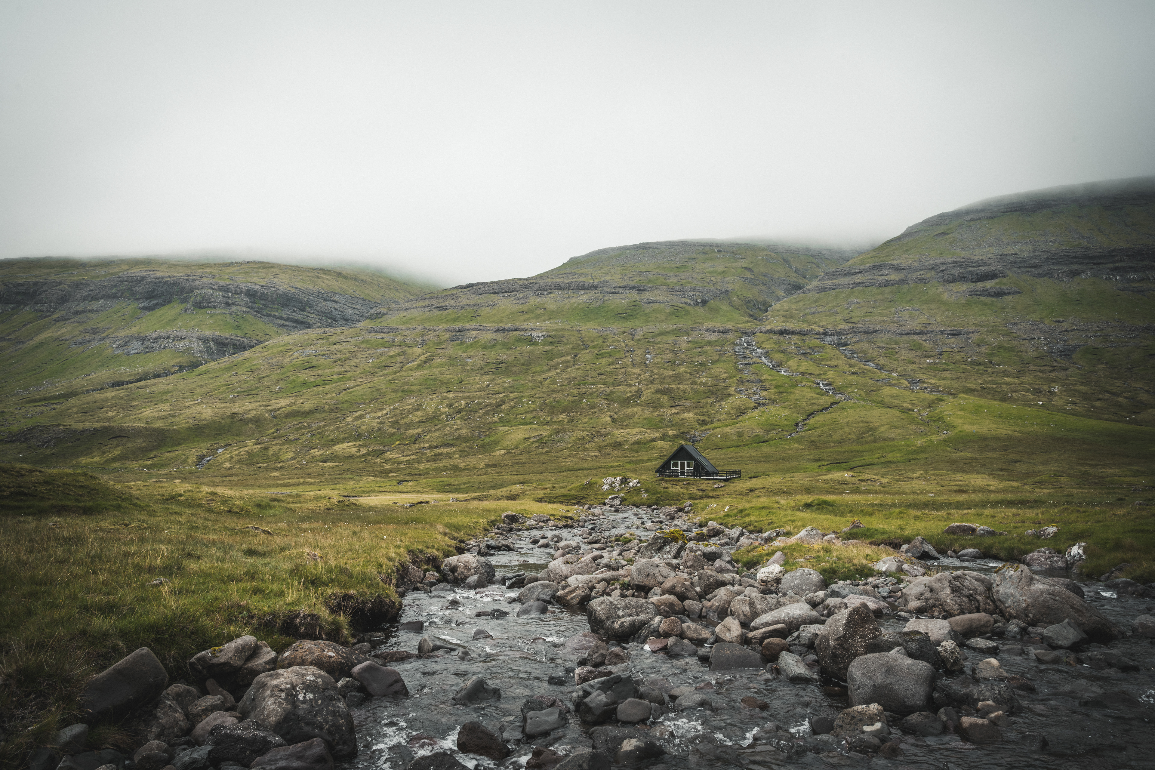 A stream traces the valley floor toward a distant structure. The route is clear, the destination deliberately uncertain.