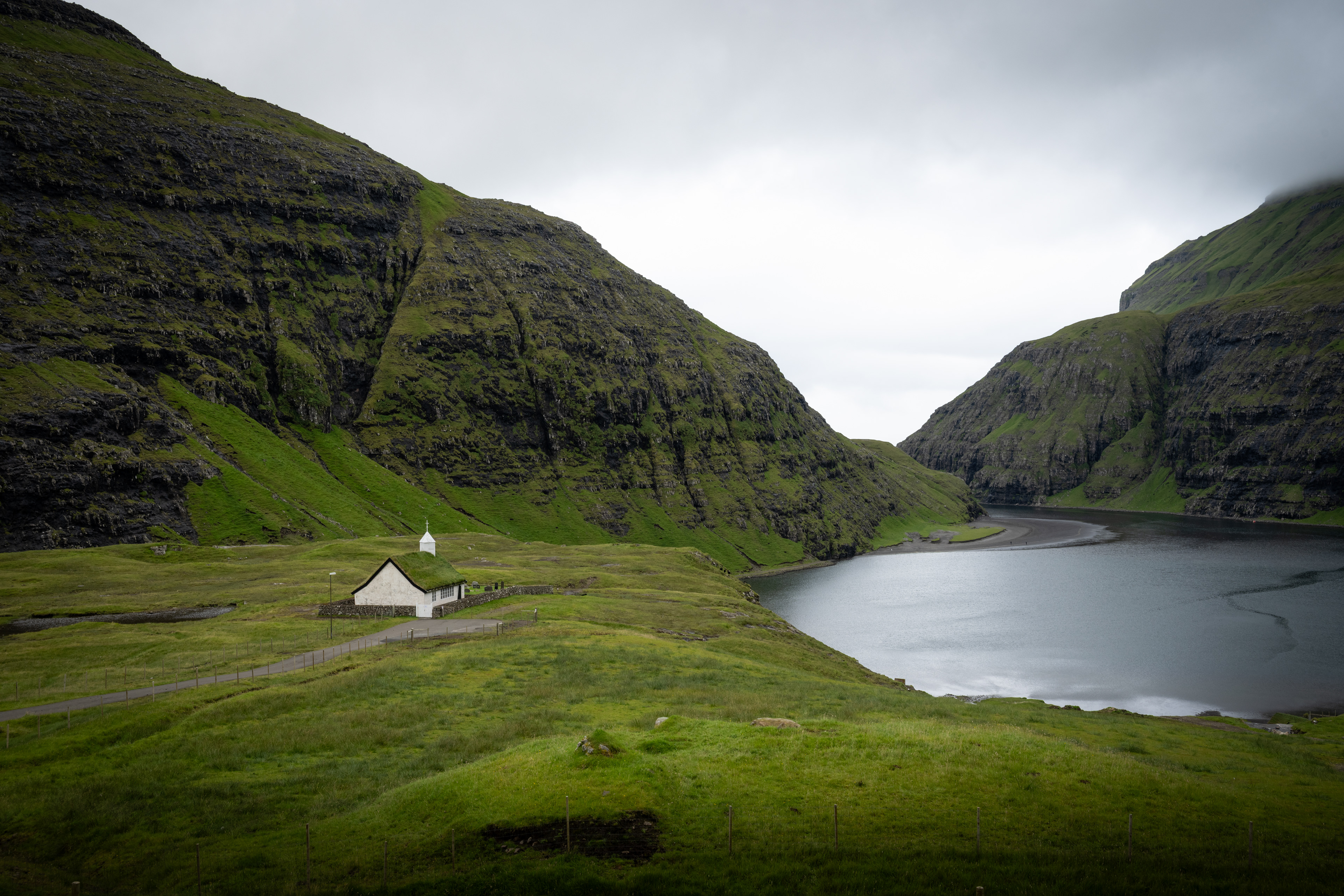 Land, water, and structure share the same narrow margin. Nothing asserts itself; the valley sets the terms and holds them in place.