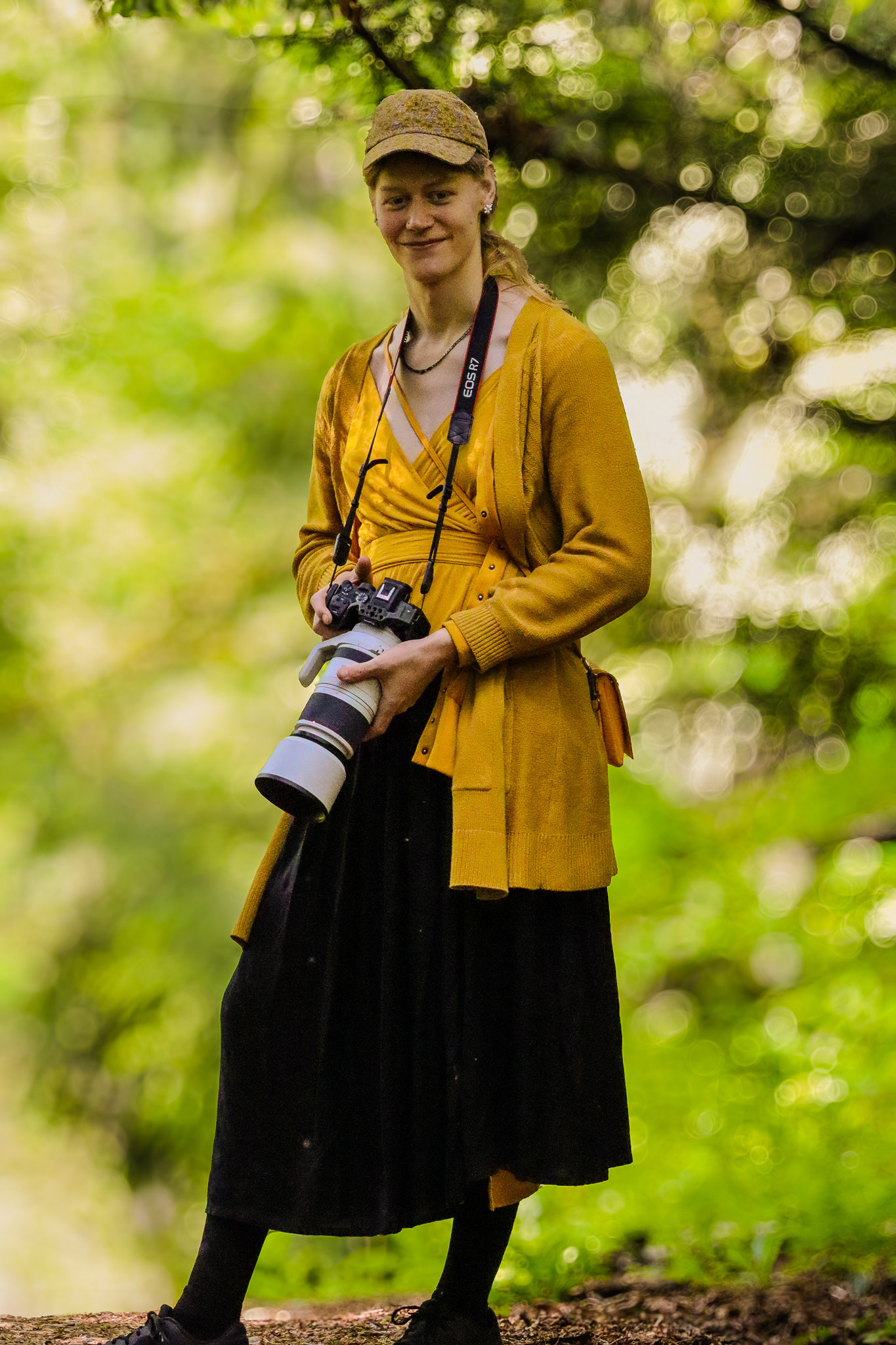 Photo of Beatrix Blair standing in the forest holding a camera.